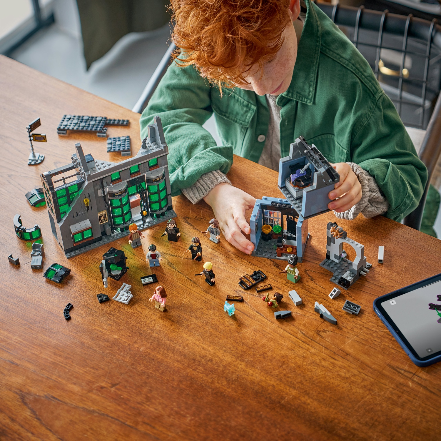 Un bambino costruisce un set Lego di un edificio con finestre verdi e molte minifigure.