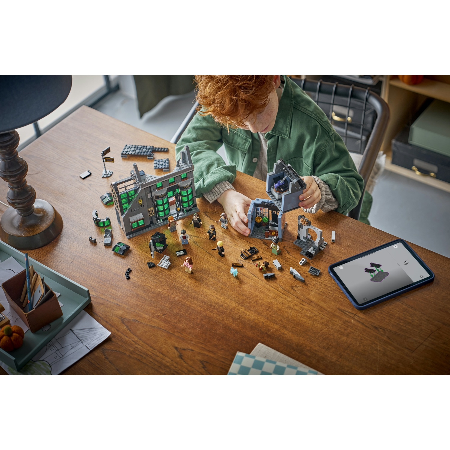 Ragazzo costruisce set Lego con istruzioni su tablet su tavolo di legno. Pezzi e figure Lego sparsi.