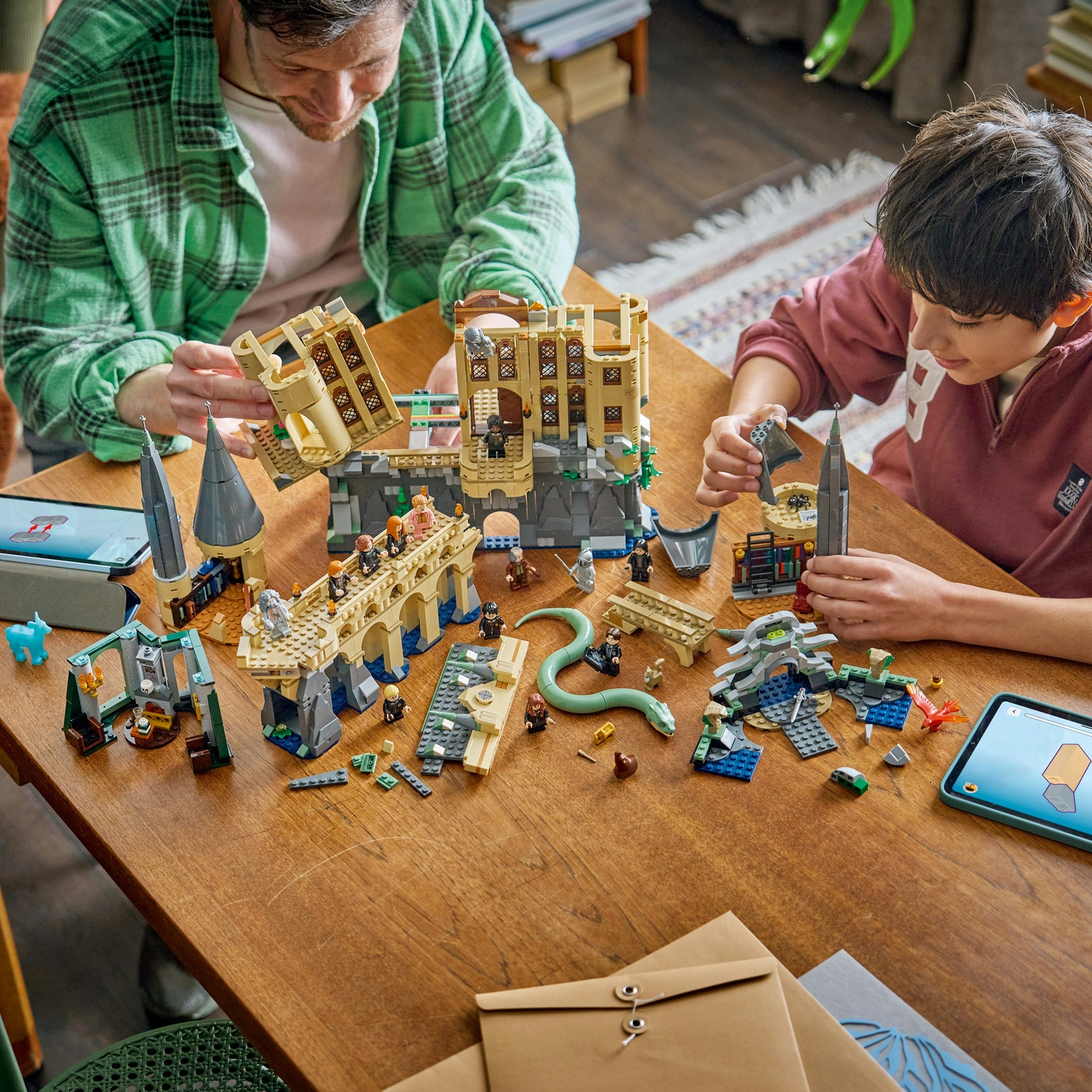 Padre e figlio costruiscono un set di castello Lego su tavolo di legno. Visibili castello, ponte, serpente e figure.