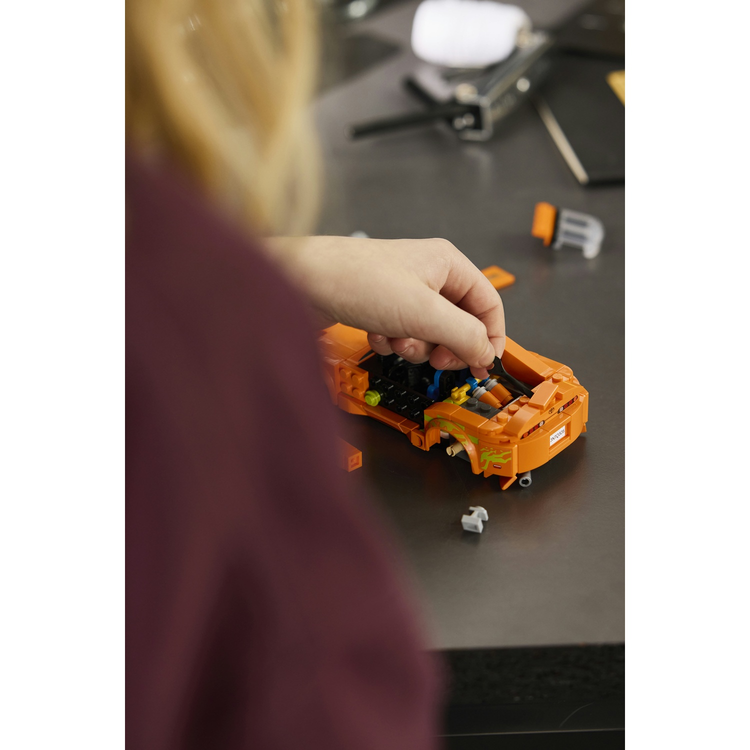 Un bambino sta assemblando un'auto da corsa Lego arancione su un tavolo.