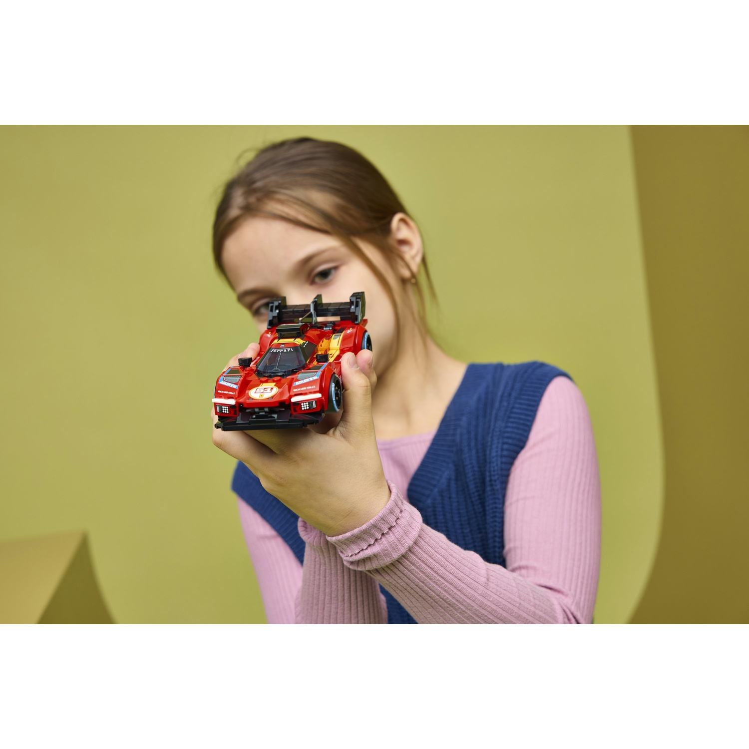 Una ragazza tiene un'auto Lego rossa con ali su sfondo giallo.