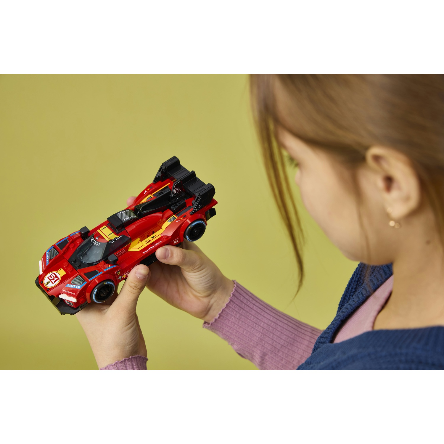 Un bambino tiene un'auto da corsa Lego rossa con accenti gialli su sfondo giallo.