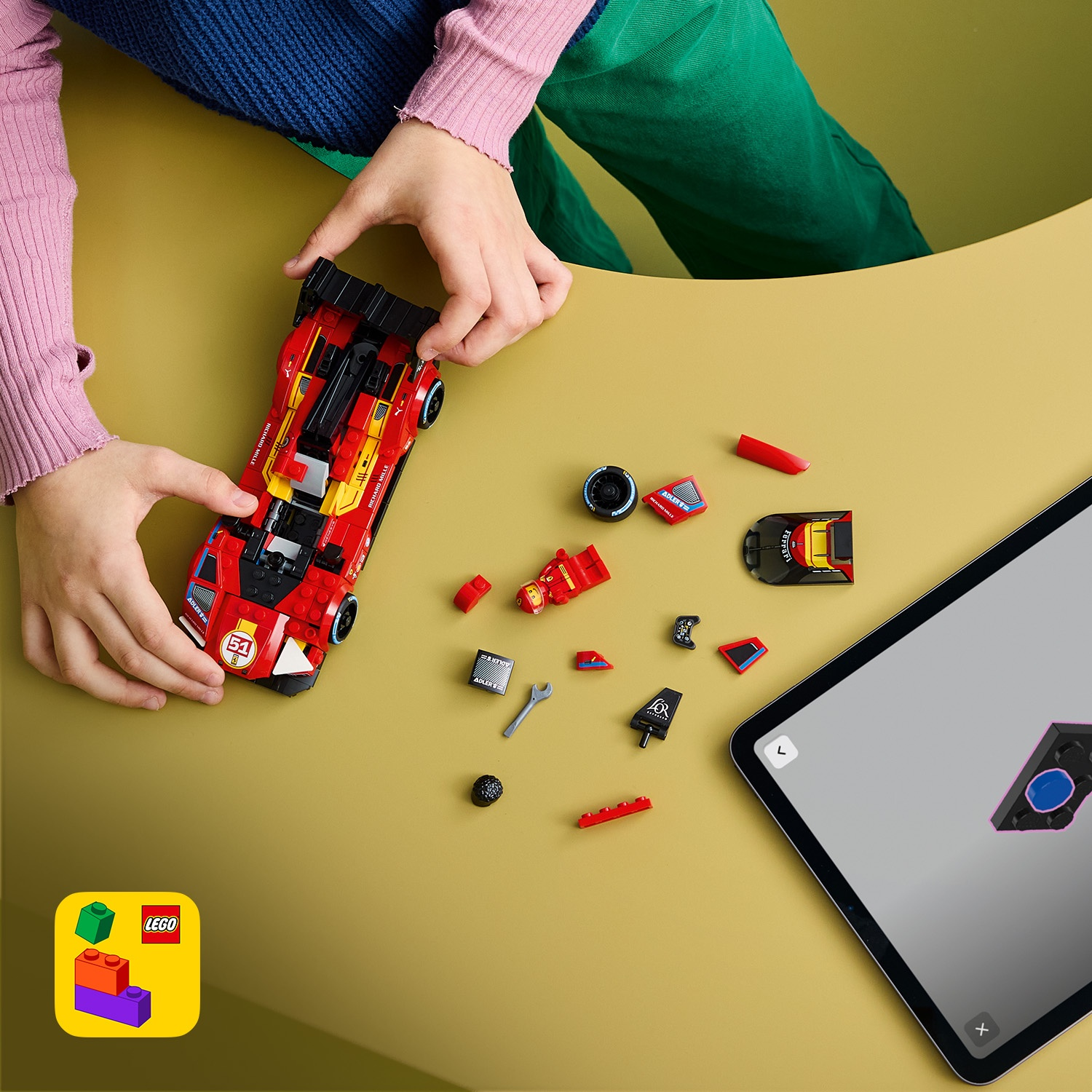 Mani assemblano un kit di auto Lego rosso accanto a un tablet che mostra istruzioni e pezzi sparsi.