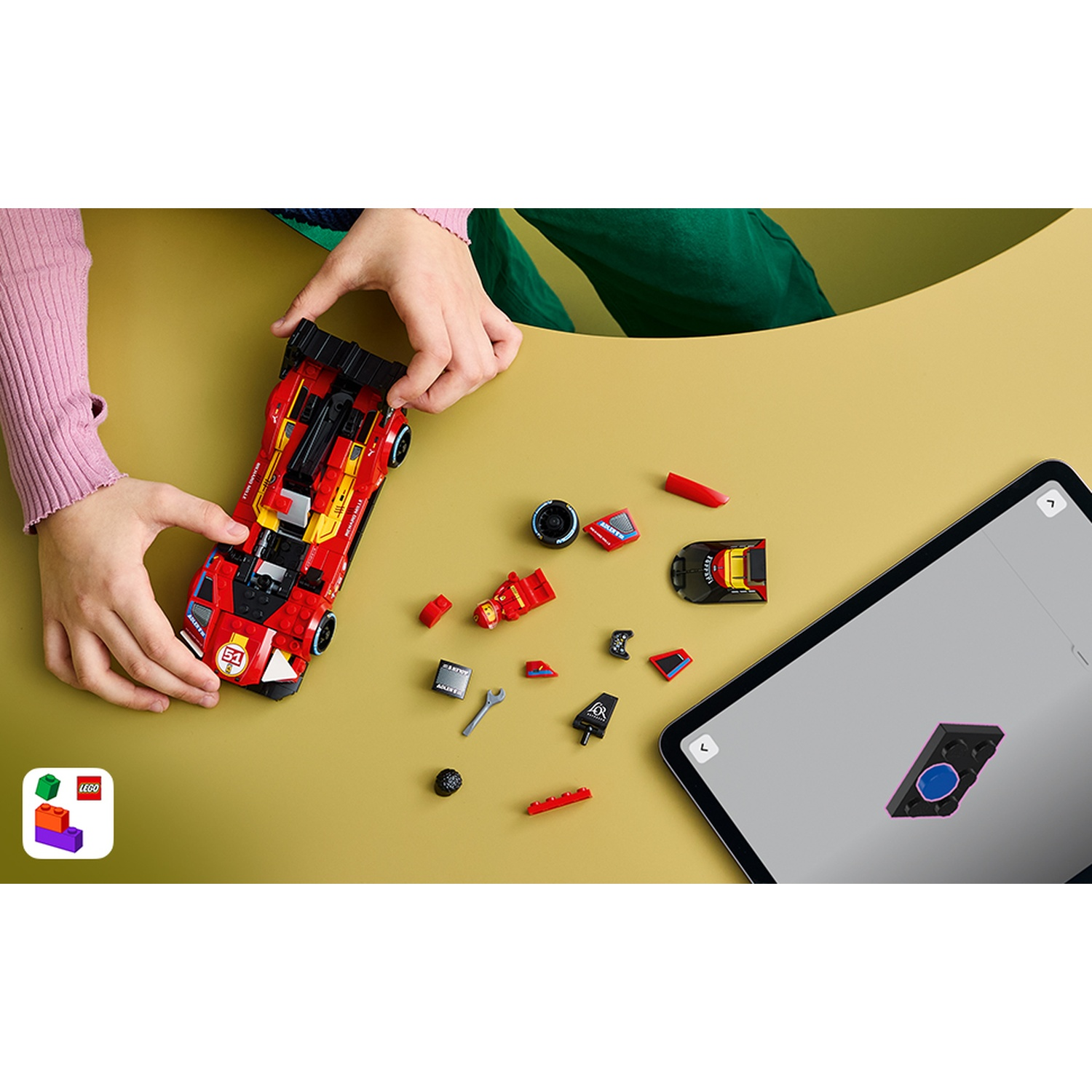 Mani che assemblano un'auto da corsa Lego rossa. Pezzi e tablet nelle vicinanze.