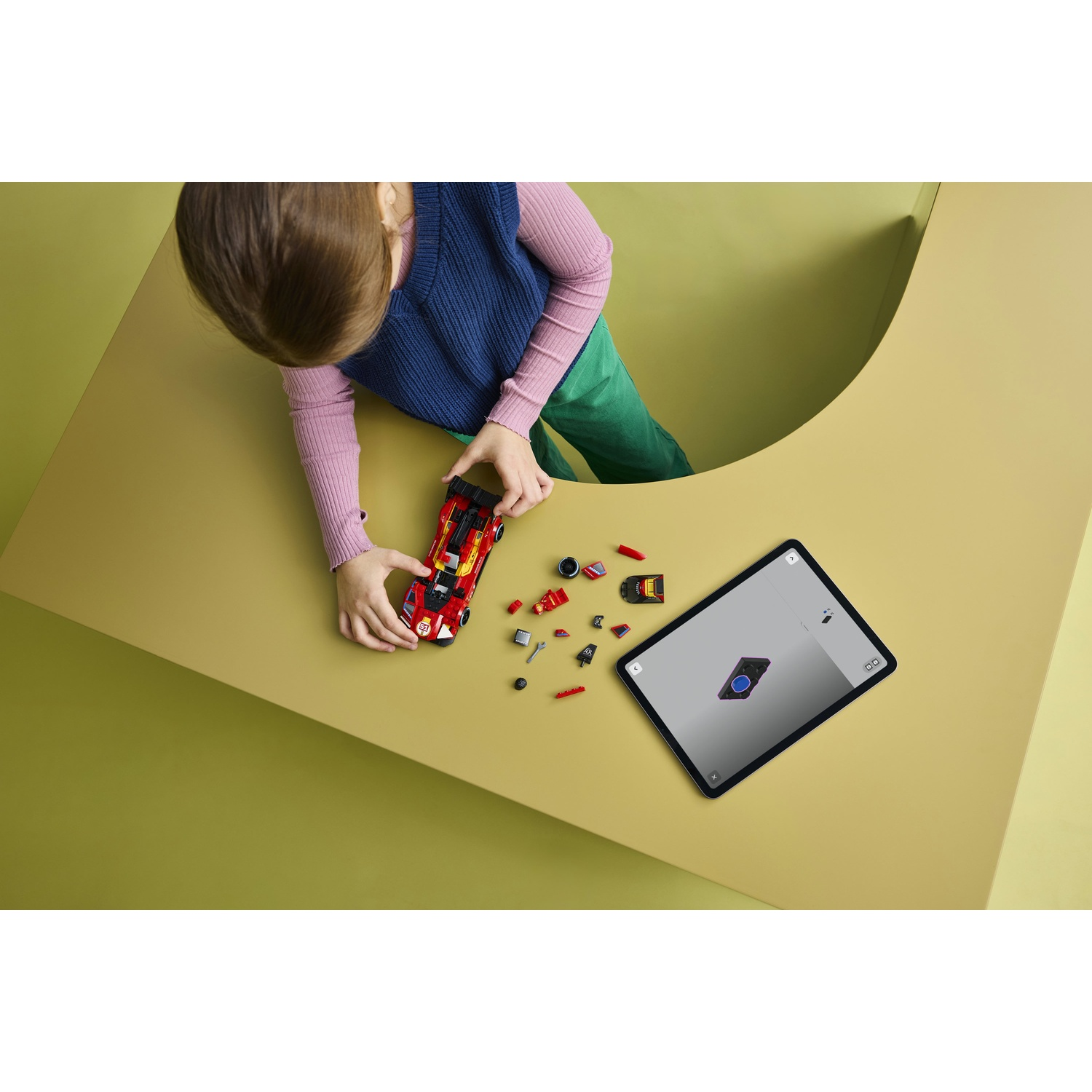 Un bambino costruisce un'auto da corsa giocattolo rossa con pezzi Lego accanto a un tablet.