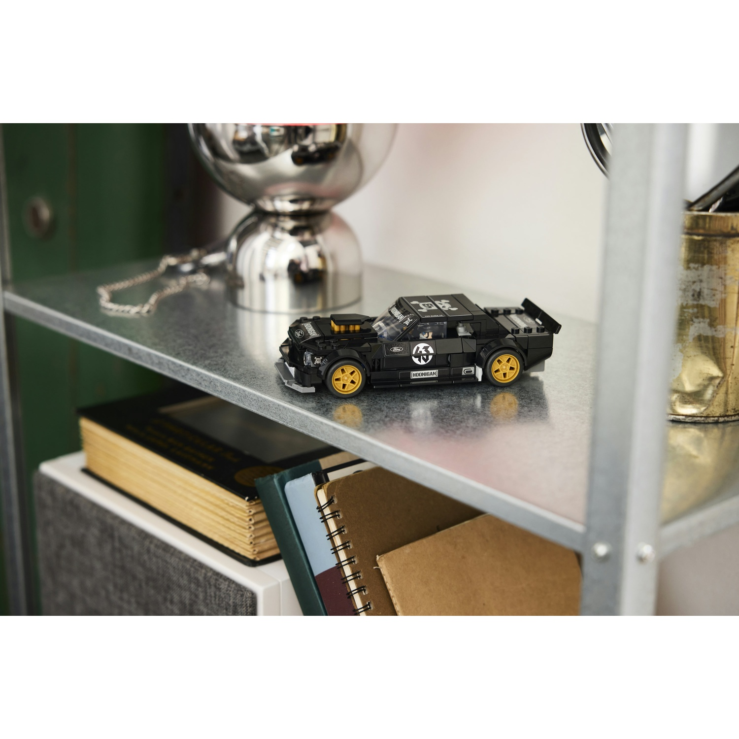 Un'auto Lego nera con ruote gialle si trova su uno scaffale accanto ai libri.