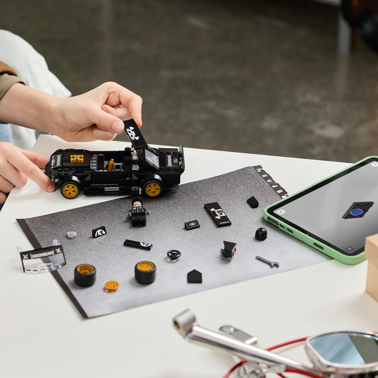Una persona costruisce un'auto Lego nera con ruote gialle. Pezzi sul tavolo.