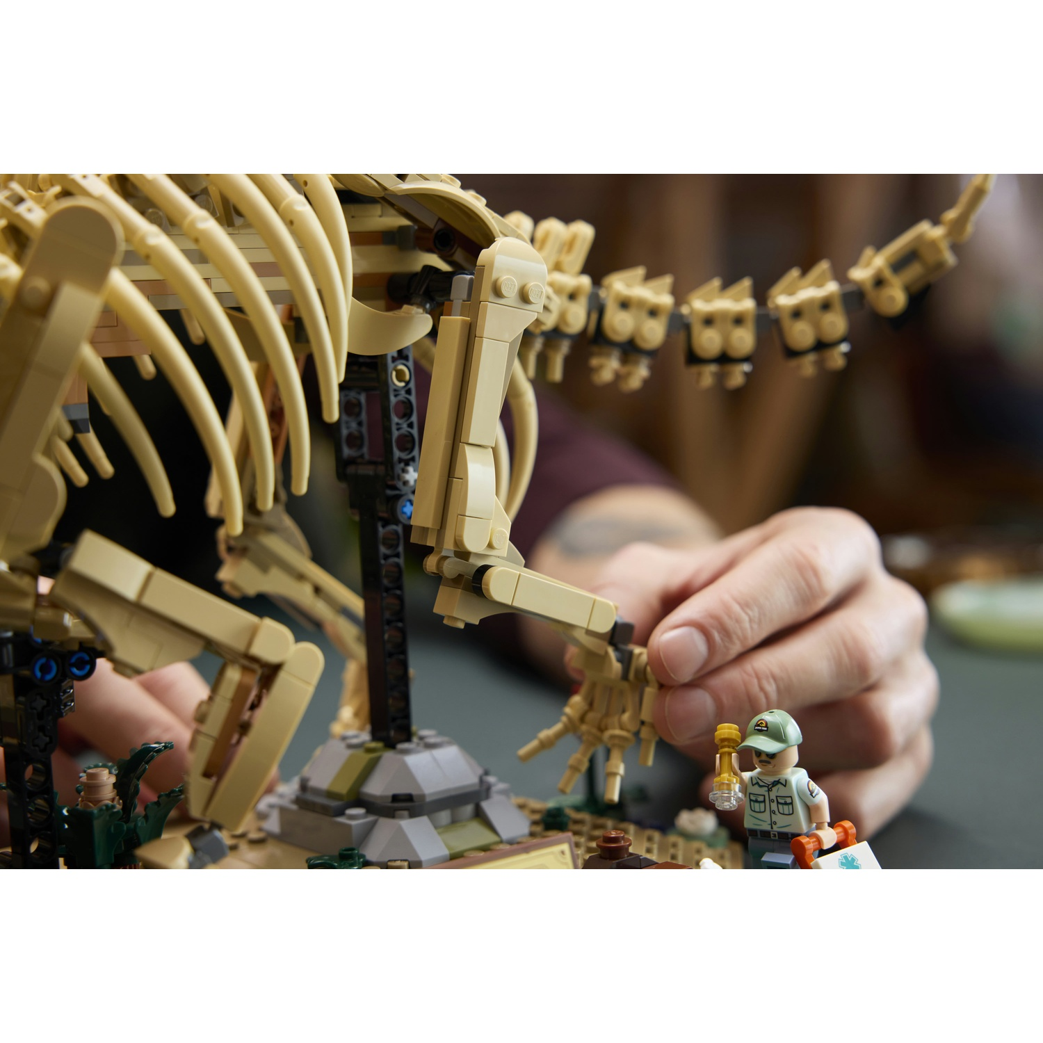Una mano costruisce uno scheletro di dinosauro Lego con un archeologo figura di dinosauro.