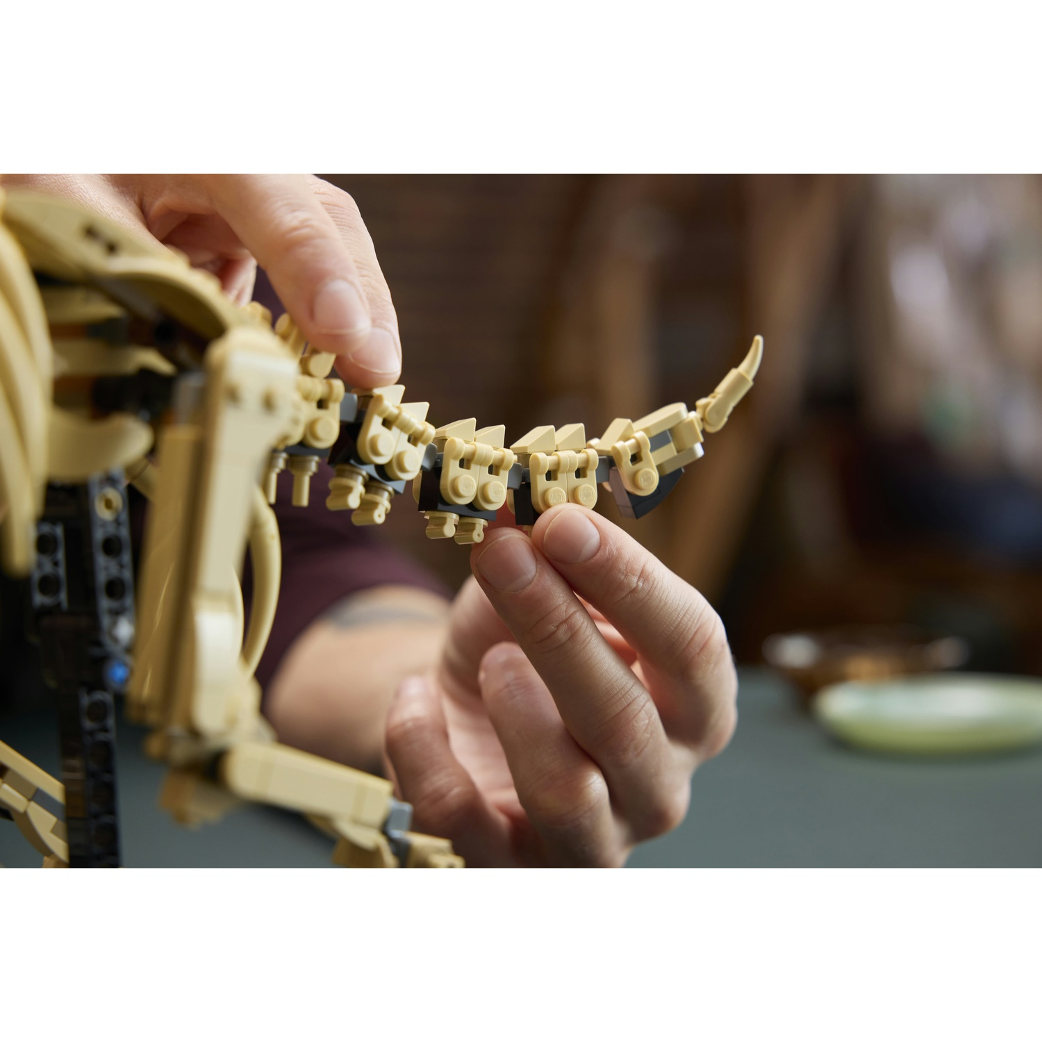 Mani che assemblano un droide Lego beige. Inserimento della sezione della coda.