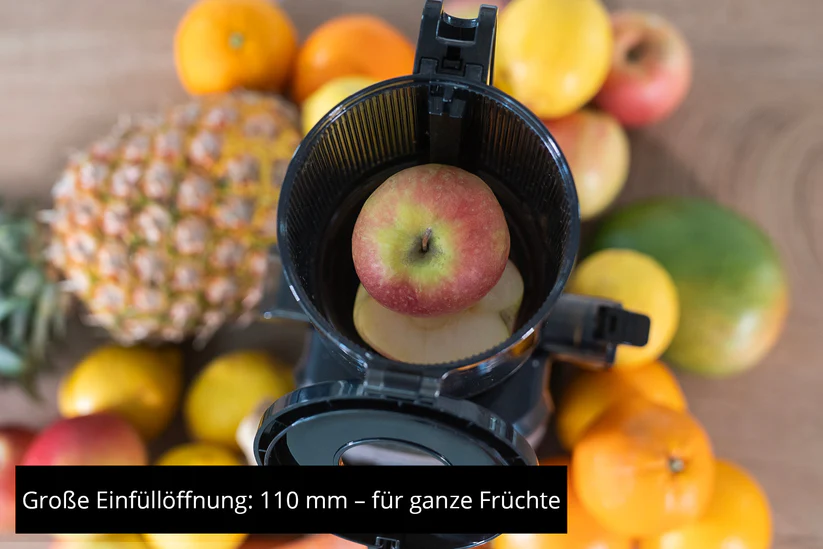 Ein Apfel in einem Entsafter mit Früchten wie Ananas, Orangen und Zitronen.