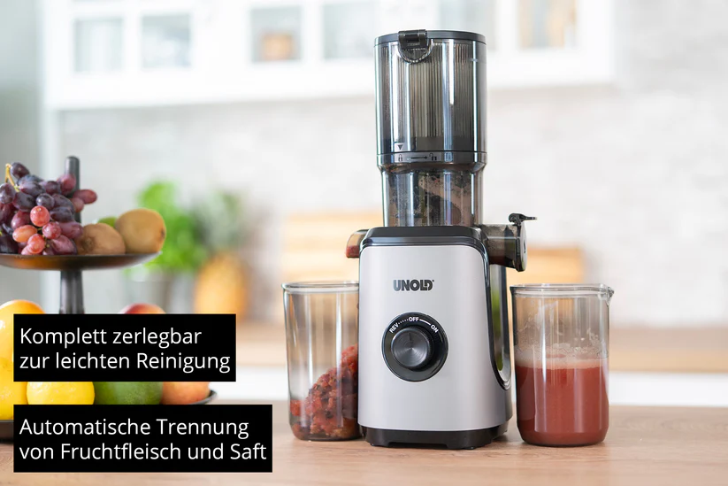 Ein silberner Entsafter mit Beeren, Kiwis und Orangensaft auf einem Holztisch.