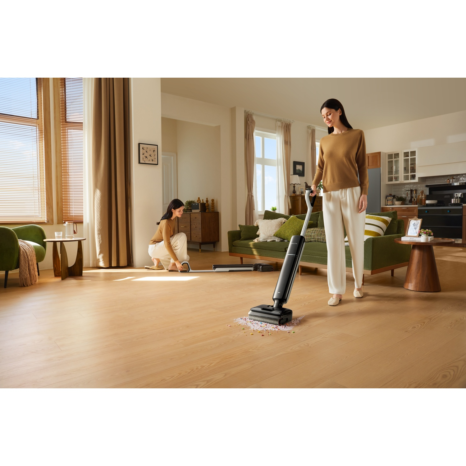 Two women clean a wooden floor with a wet dry vacuum in a bright living room.