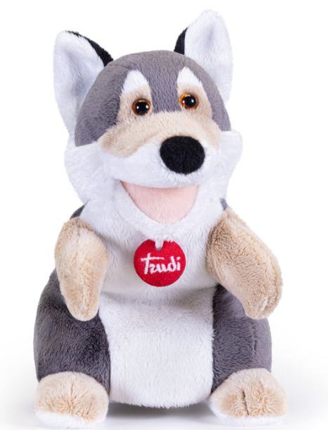 Ein flauschiges Wolf-Stofftier mit einem roten Trudi-Anhänger sitzt.