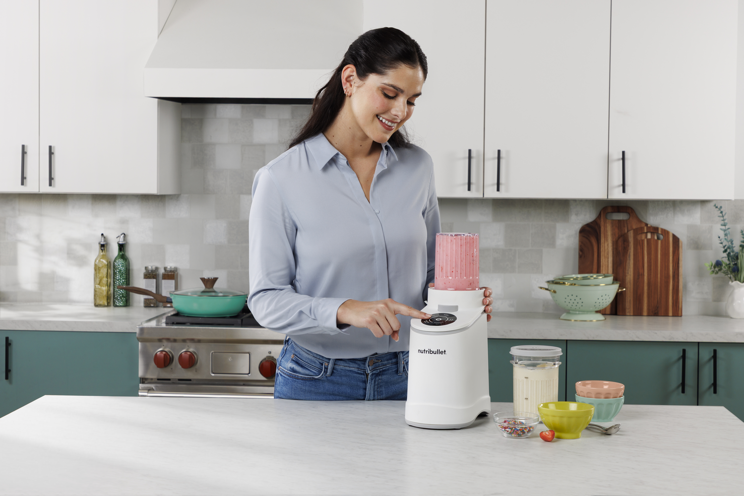 Mujer en cocina usando licuadora Nutribullet con batido rosa.