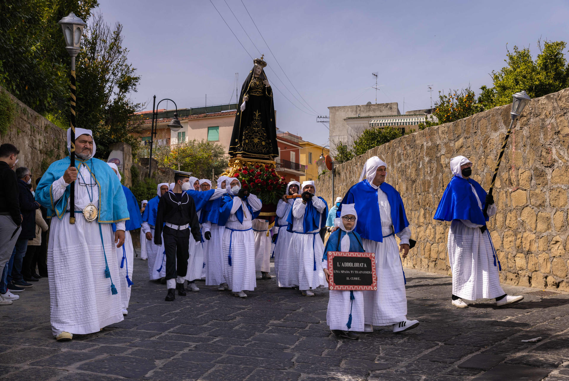 Eine Prozession mit Männern in weißen Roben und blauen Umhängen trägt eine Statue.