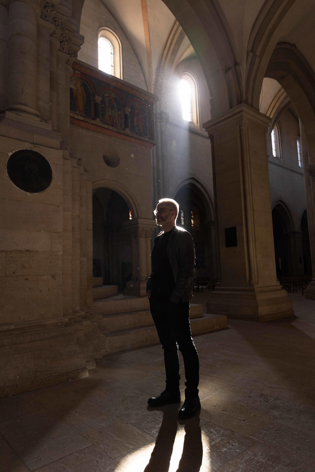 Ein Mann steht in einer Kathedrale im Lichtstrahl. Staubpartikel schweben.