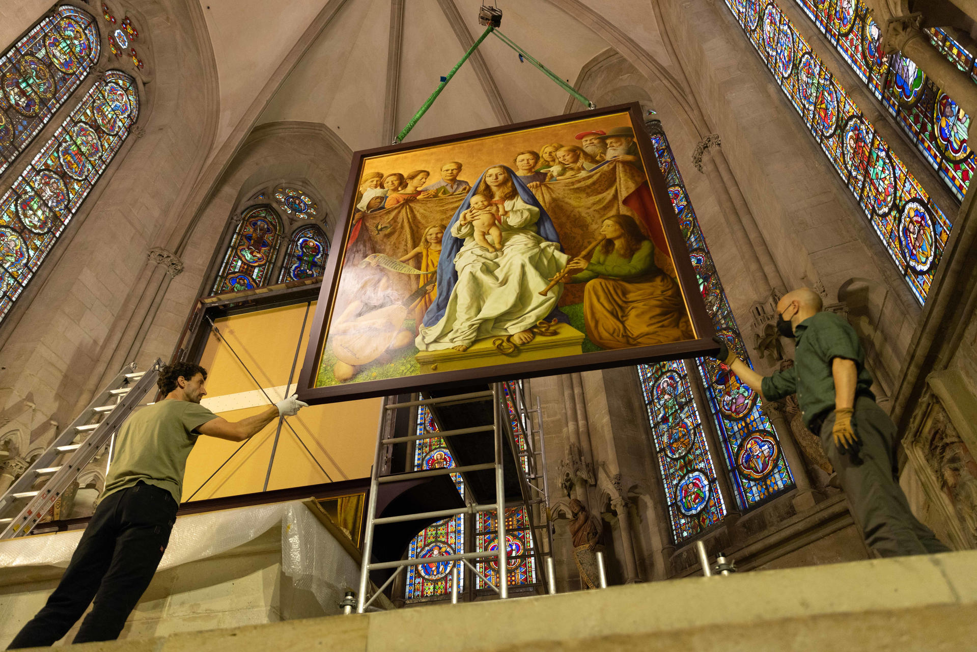 Männer hängen ein großes Gemälde in einer Kirche auf, mit Buntglasfenstern.