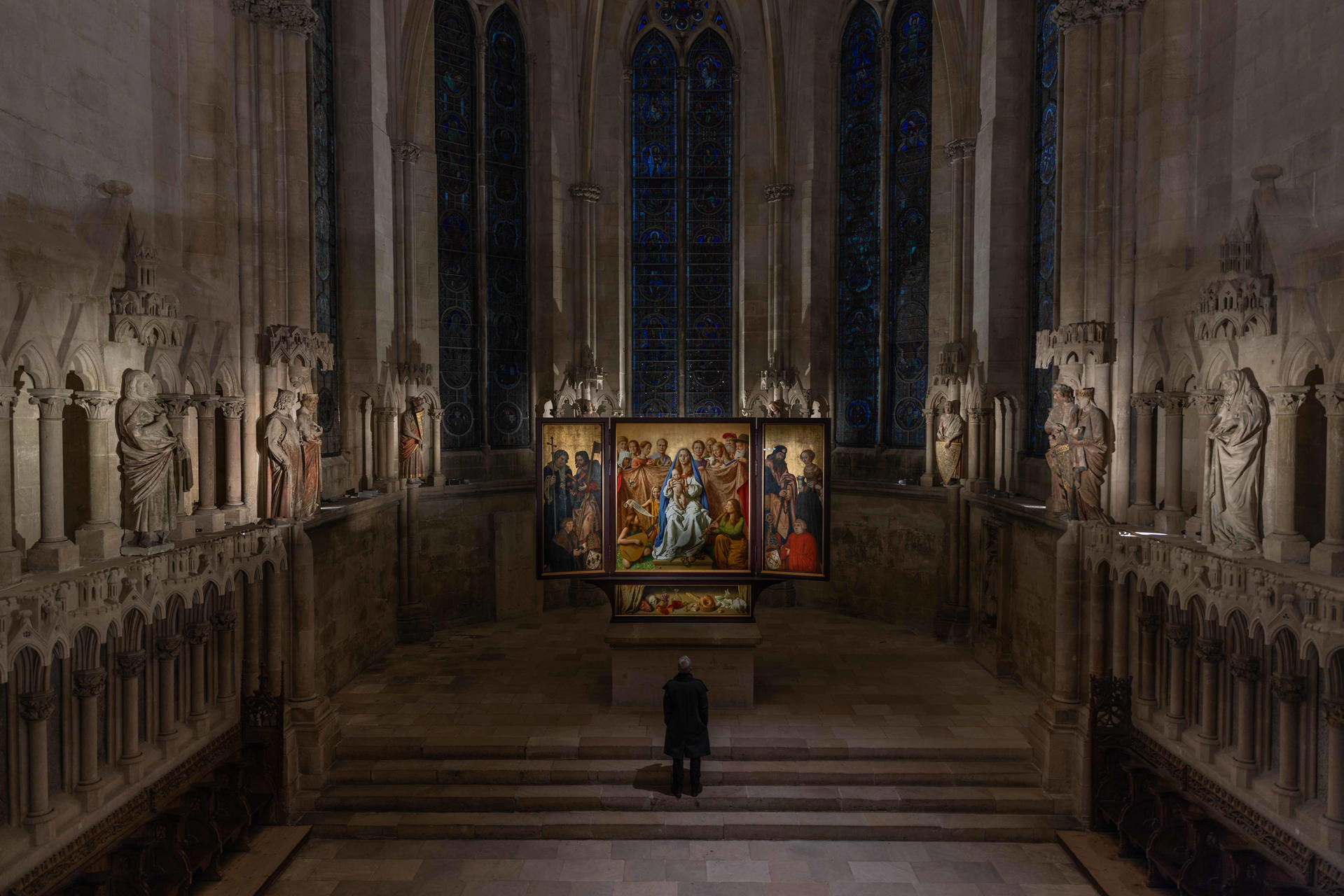 Ein Mann steht vor einem Triptychon in einer Kathedrale mit Buntglasfenstern und Statuen.