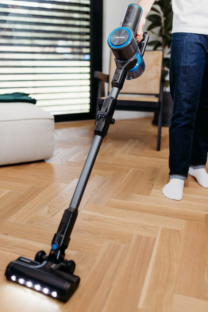 Osoba odkurza drewnianą podłogę odkurzaczem bezprzewodowym z lampkami LED.