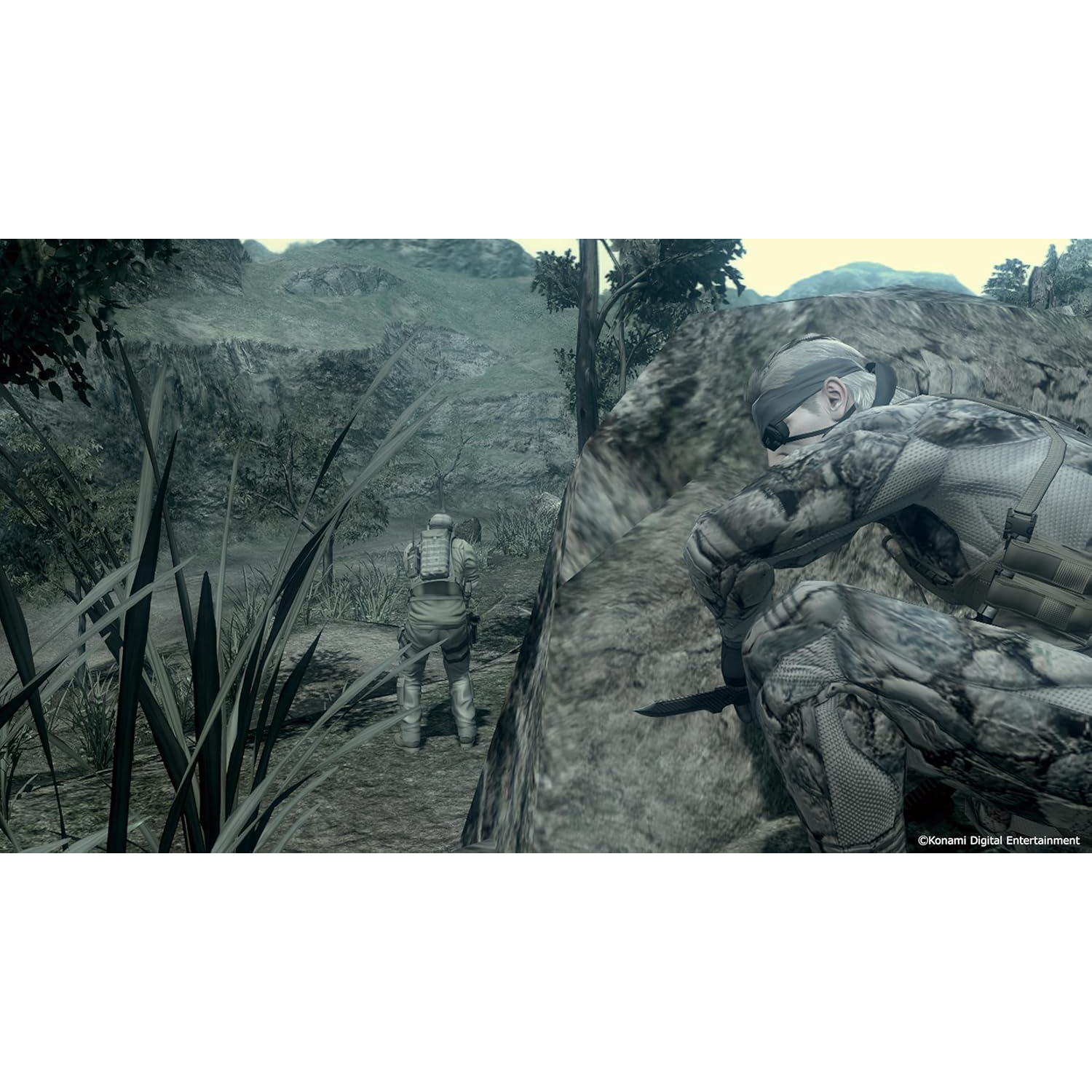 Twee soldaten in camouflage in een groen, bergachtig landschap. Eén knielt op de voorgrond, de ander staat verder weg.
