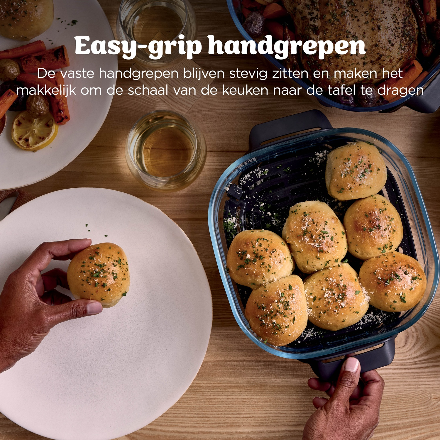 Une main tient un petit pain sur une assiette. Un plat de cuisson avec des petits pains est visible.
