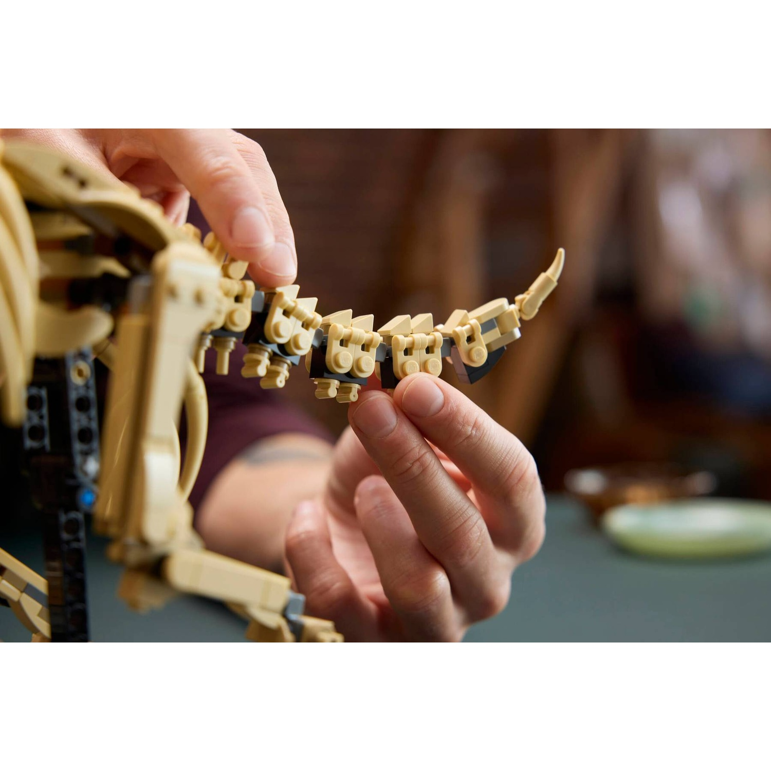 Hands assemble a tan Lego droid with black accents.