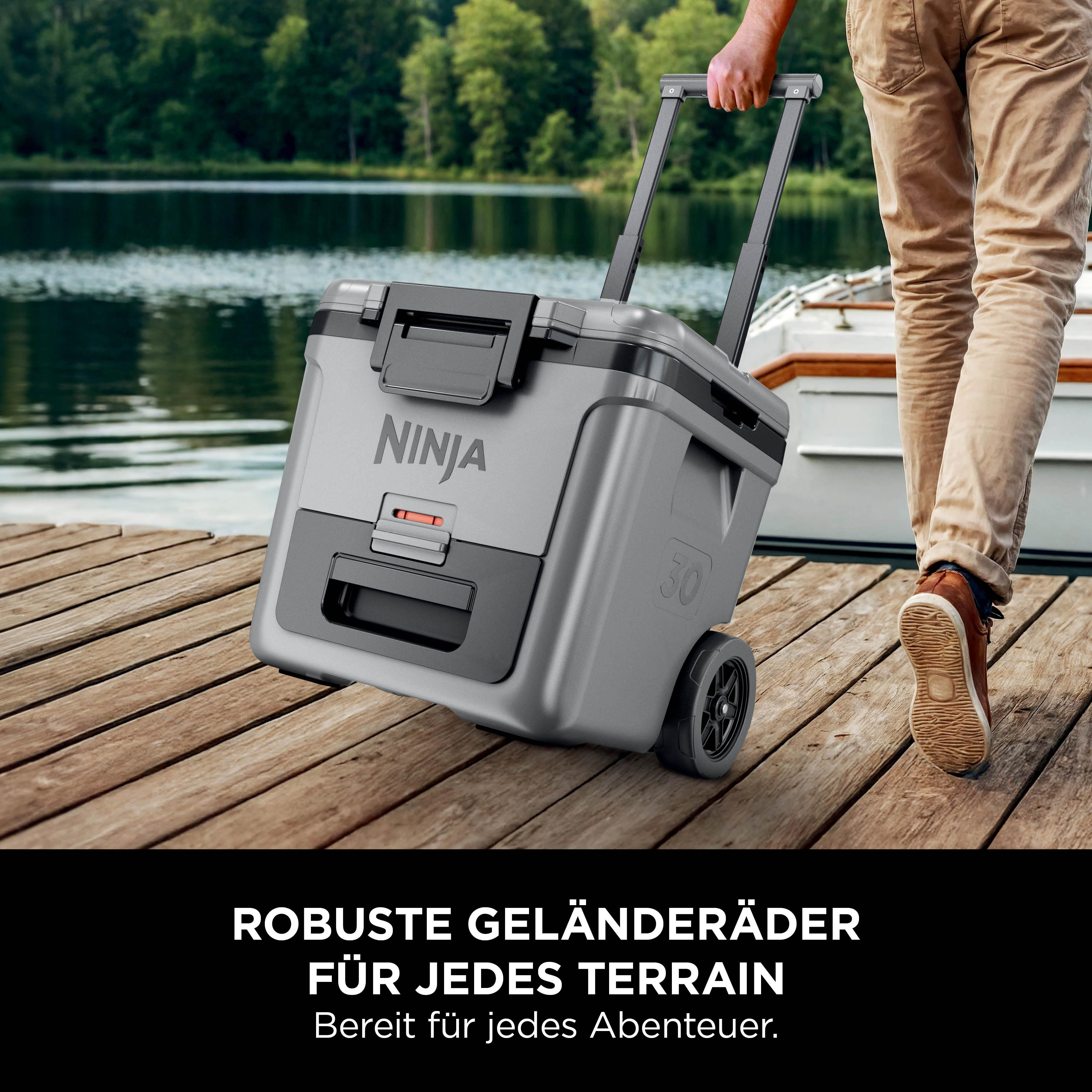Person zieht graue Ninja Kühlbox mit Rädern auf Holzsteg am See.