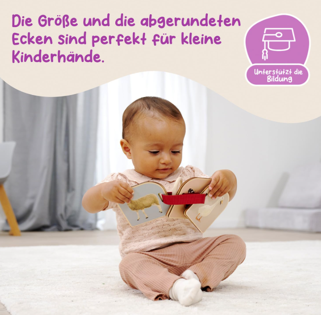 Ein Baby hält ein offenes Stoffbuch mit Tierbildern. Deutscher Text.