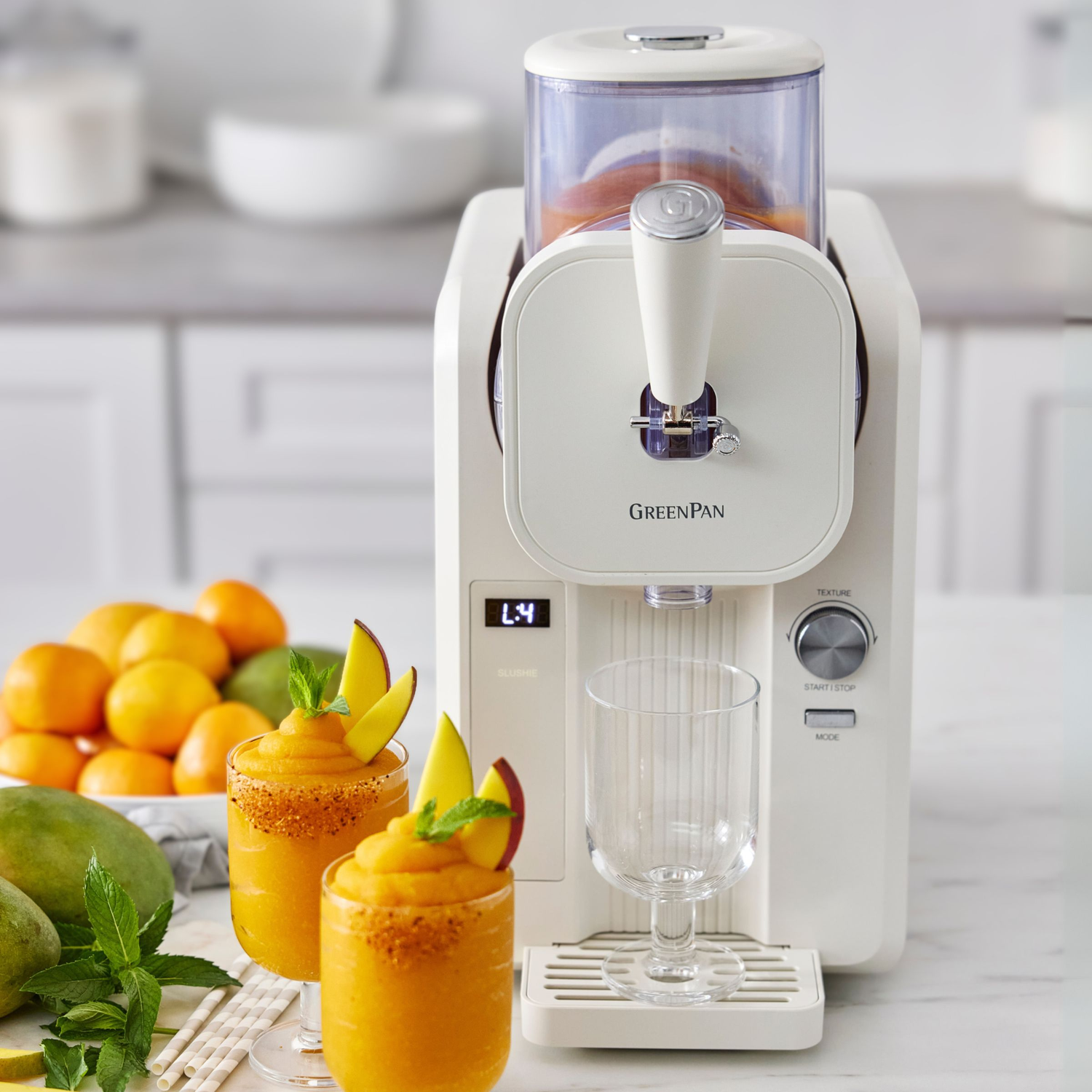 Een witte slushie-maker met twee bevroren drankjes, mango's en sinaasappels.