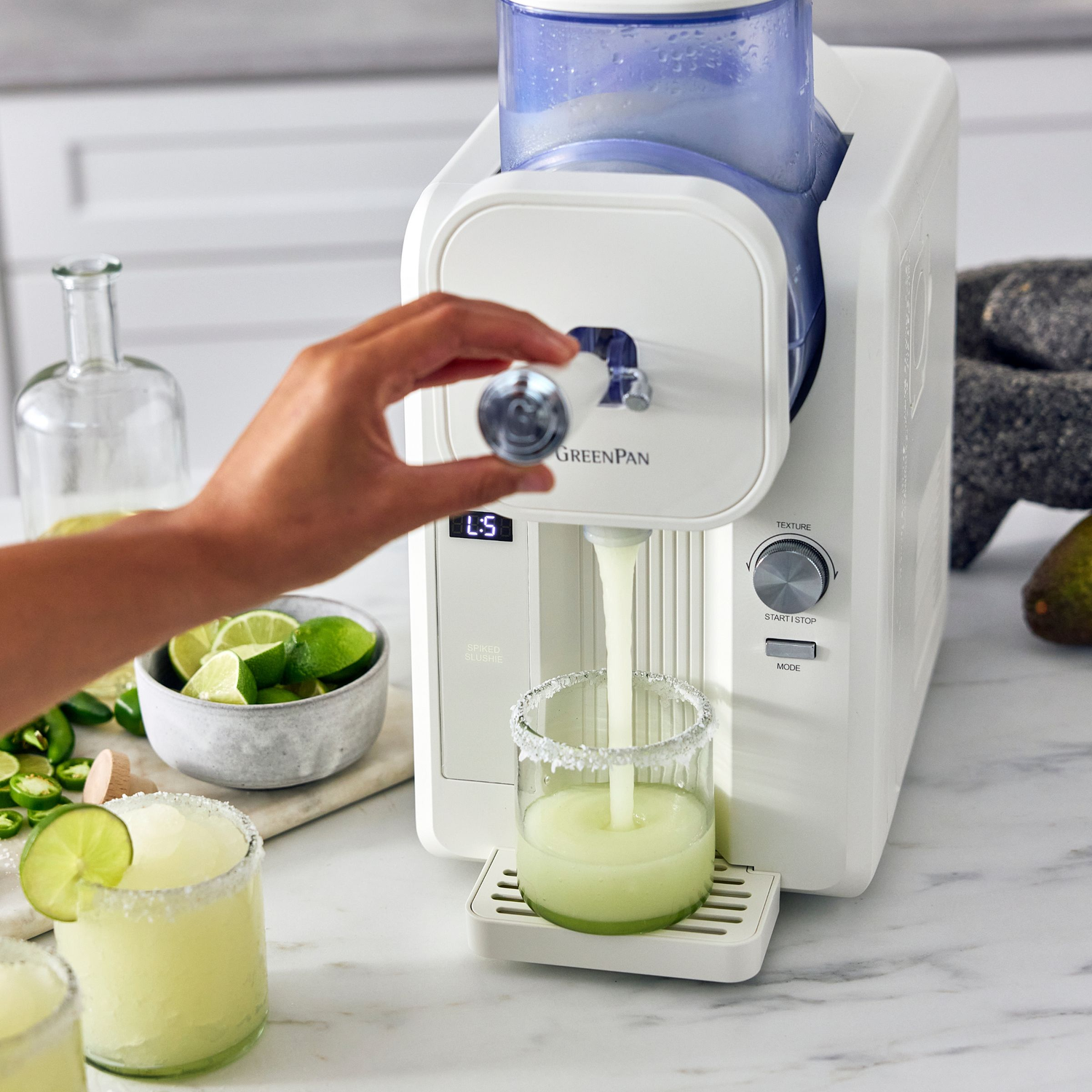 Een hand draait aan een draaiknop op een frozen drink machine terwijl een slushy in een glas met zoutrand wordt gegoten.