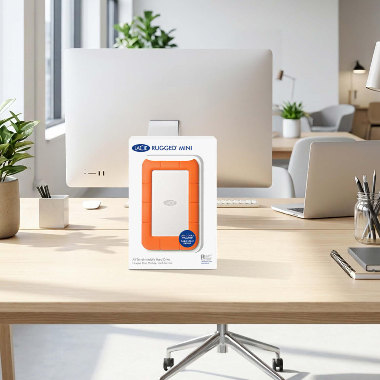 Ein orangefarbenes LaCie Rugged Mini Speichermedium auf einem Schreibtisch mit einem Computer.