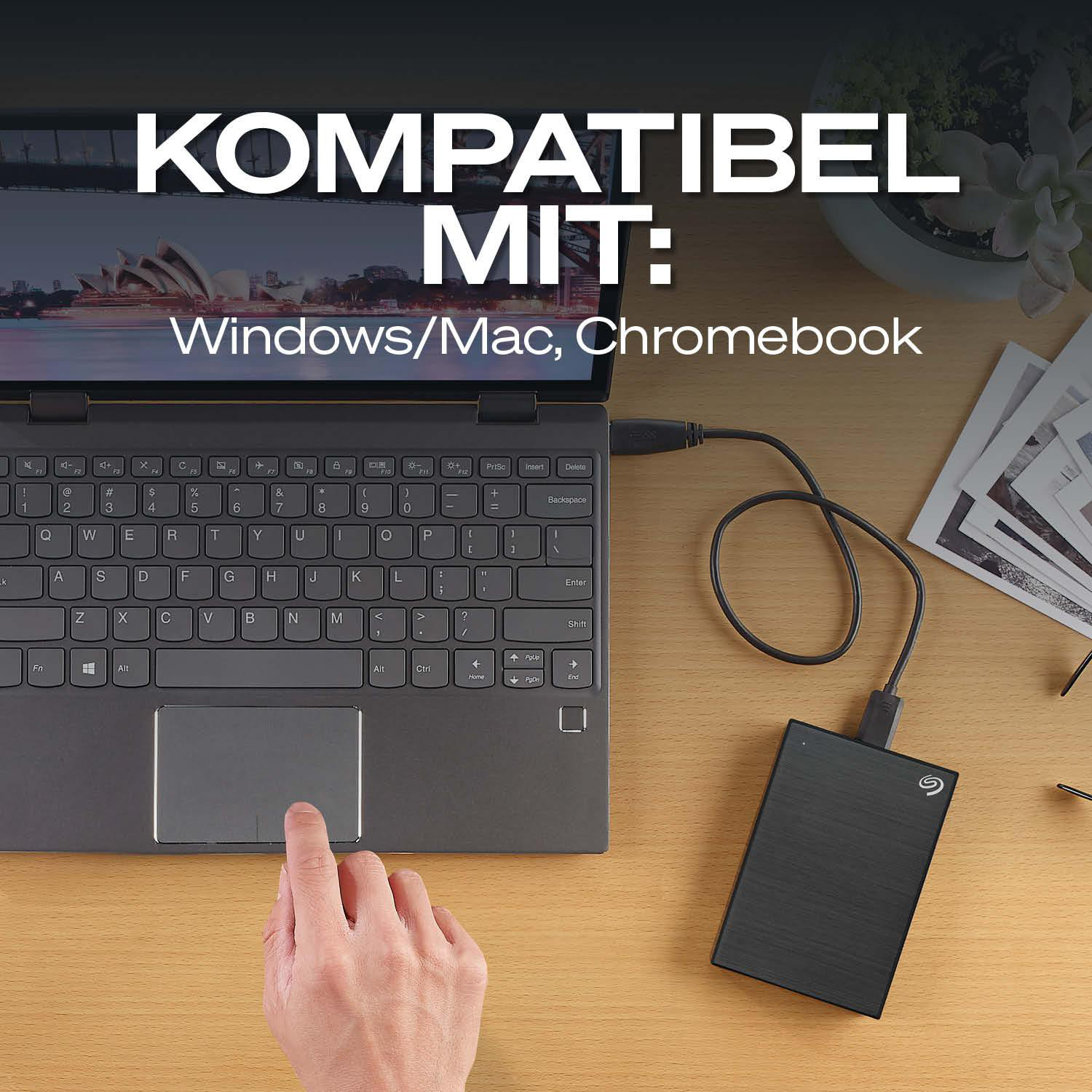 Laptop mit externer Festplatte und Fotos auf einem Schreibtisch.