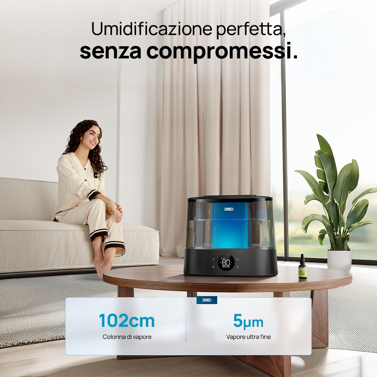 Una donna seduta su un divano accanto a un umidificatore. Un tavolo con una pianta.