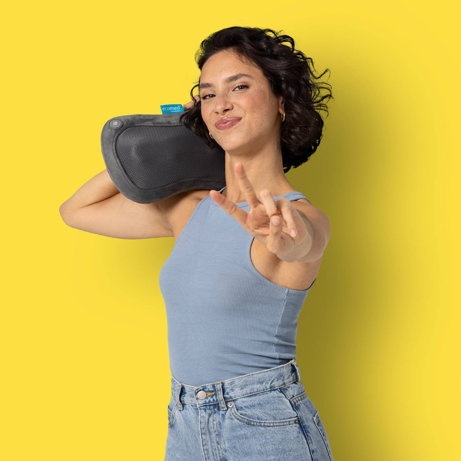 Mujer con masajeador de cuello, haciendo signo de paz sobre fondo amarillo.