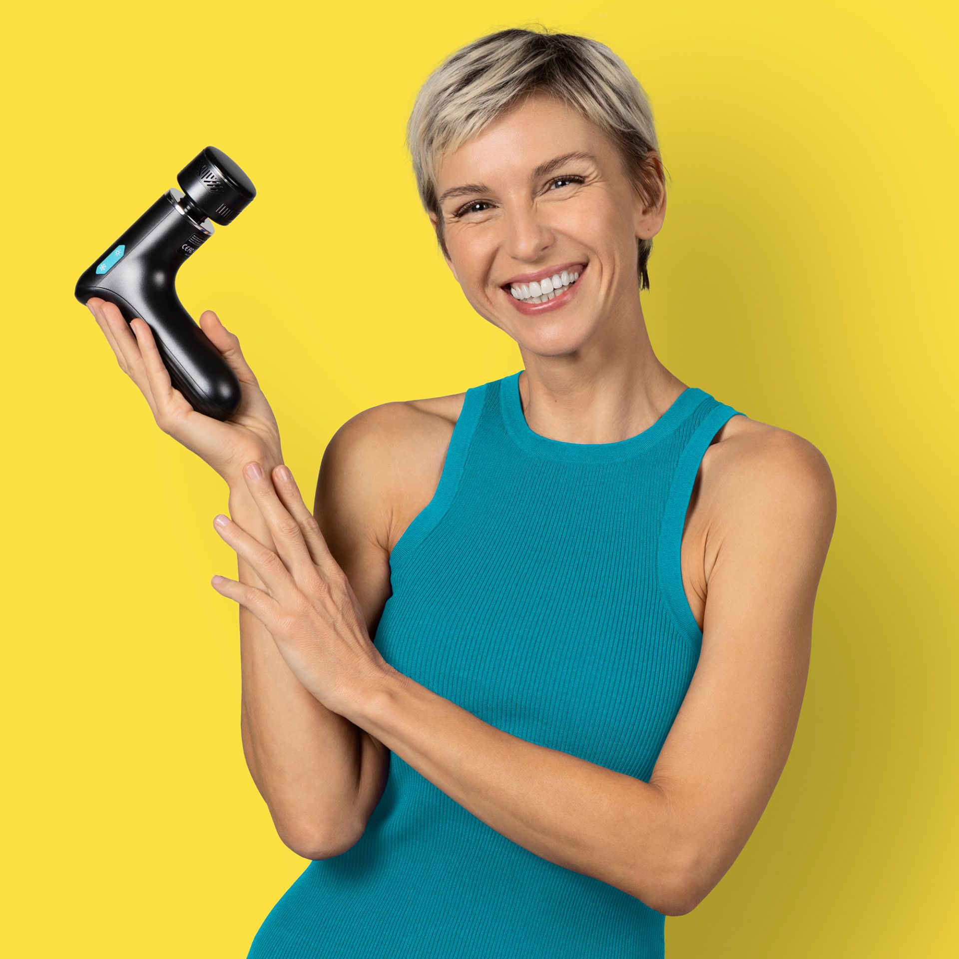 Mujer con pelo corto rubio sostiene un masajeador negro sobre fondo amarillo.