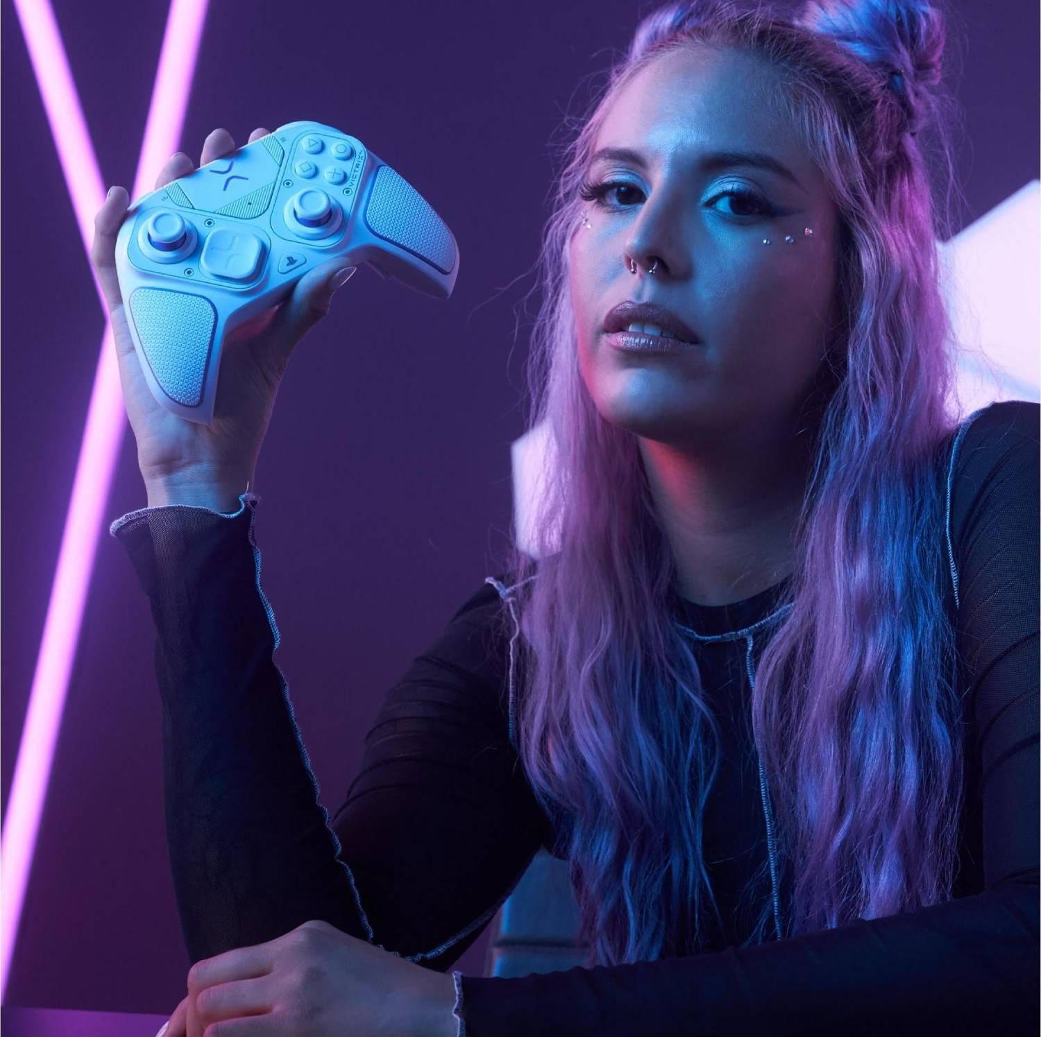 Mujer con pelo morado sostiene un mando blanco frente a luces de neón moradas.
