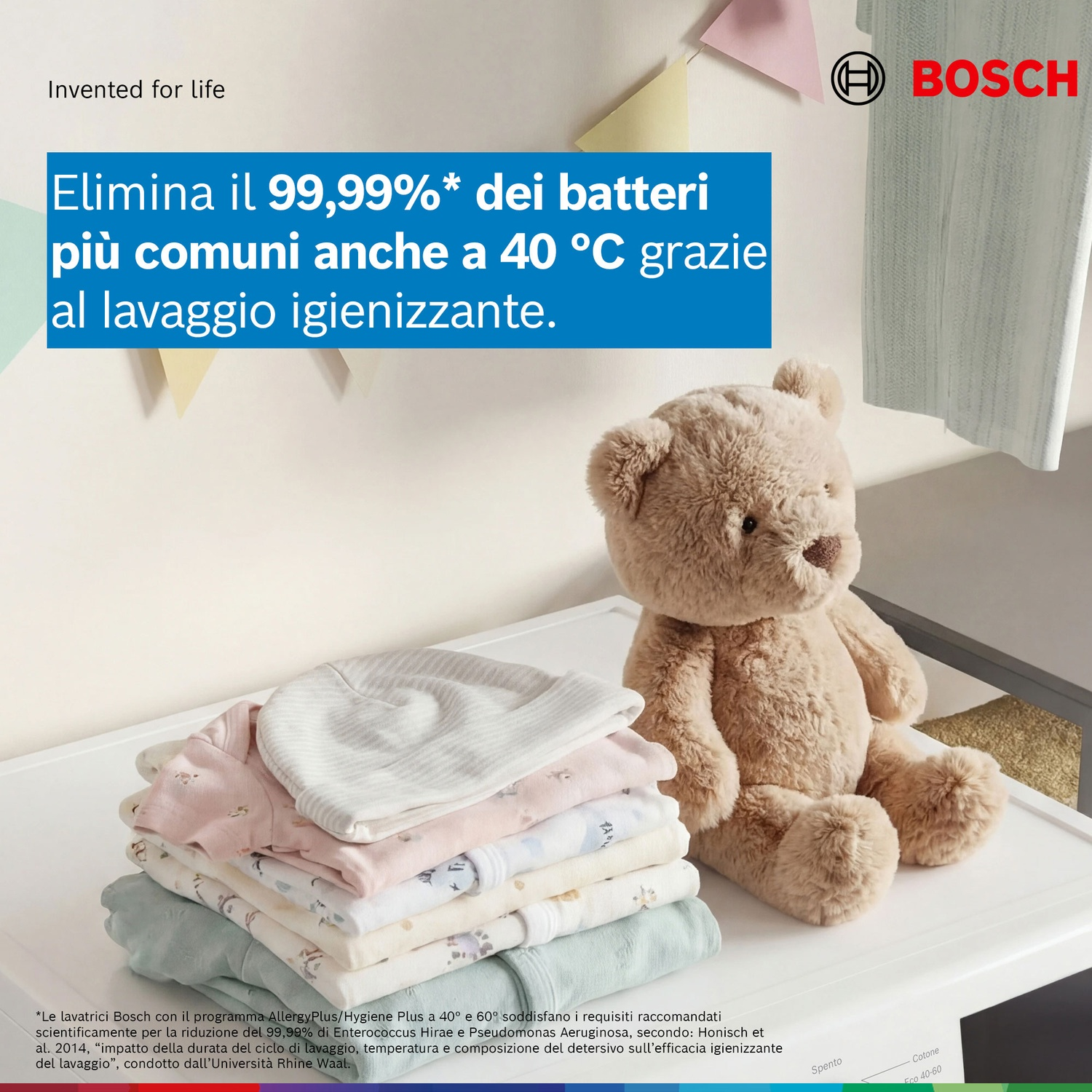 Un orsacchiotto accanto a una pila di vestiti per bambini su una lavatrice.