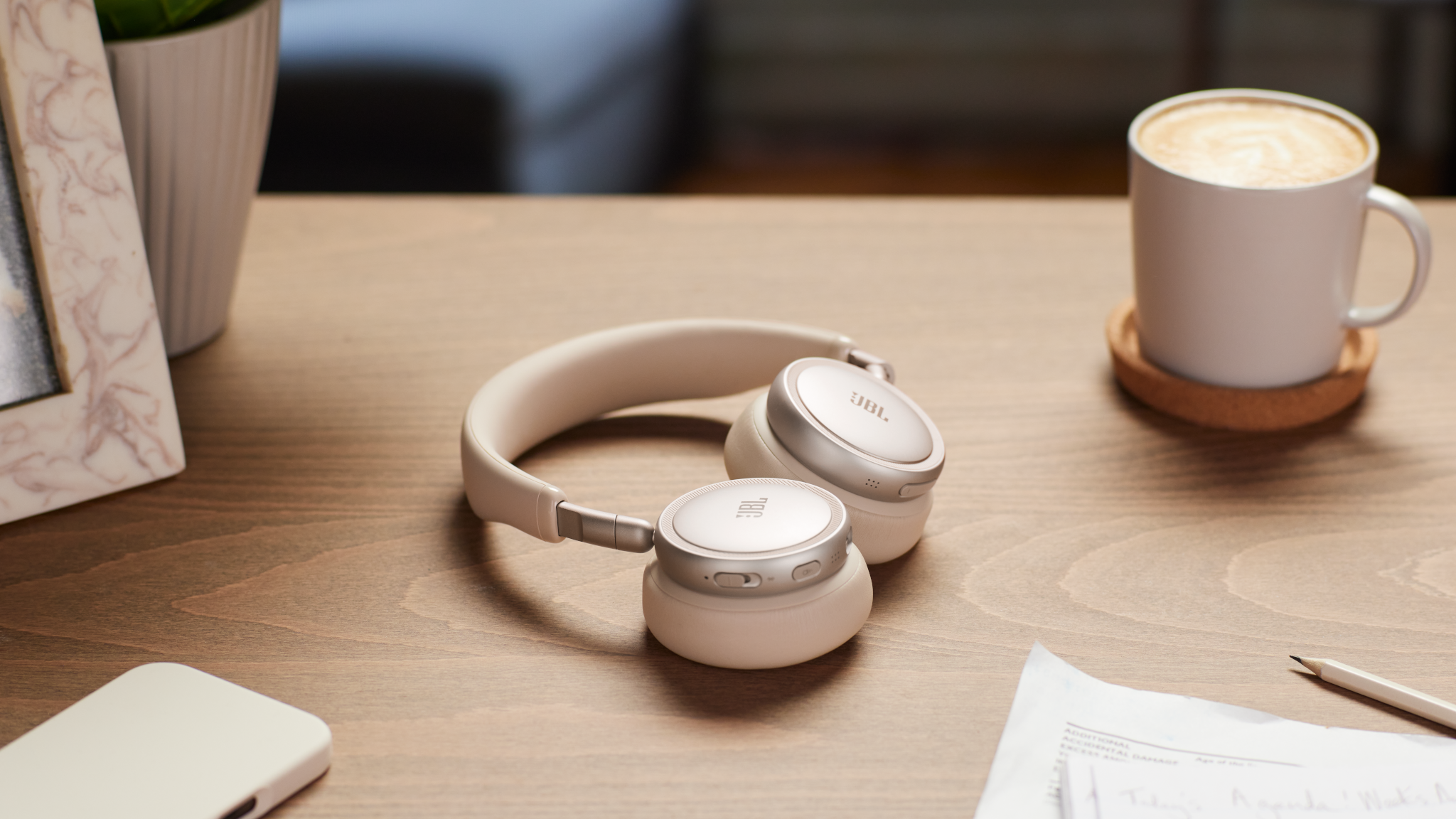 Cuffie bianche, tazza di caffè e smartphone su una scrivania di legno.
