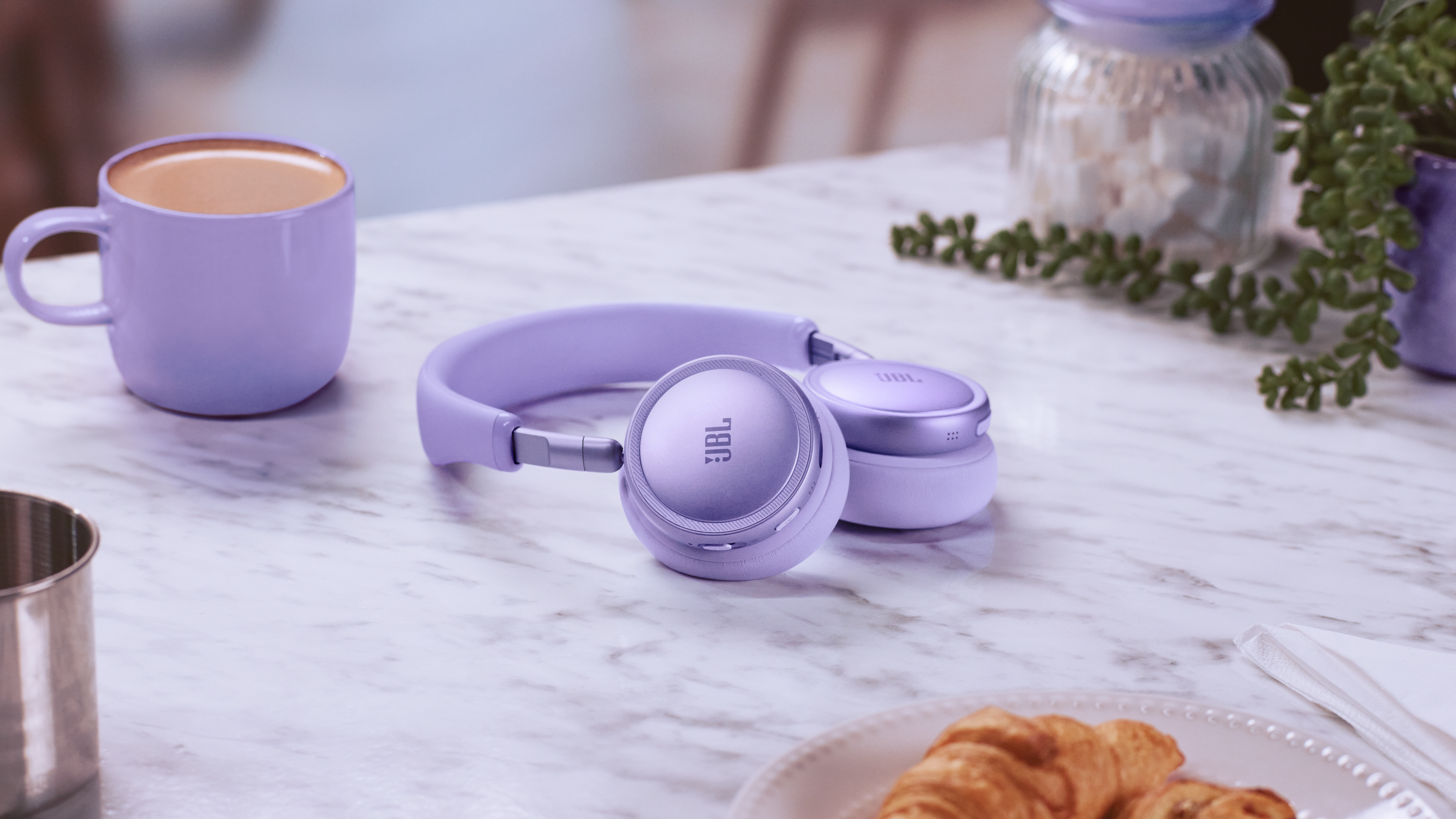 Cuffie JBL viola su tavolo di marmo con tazza di caffè e croissant.