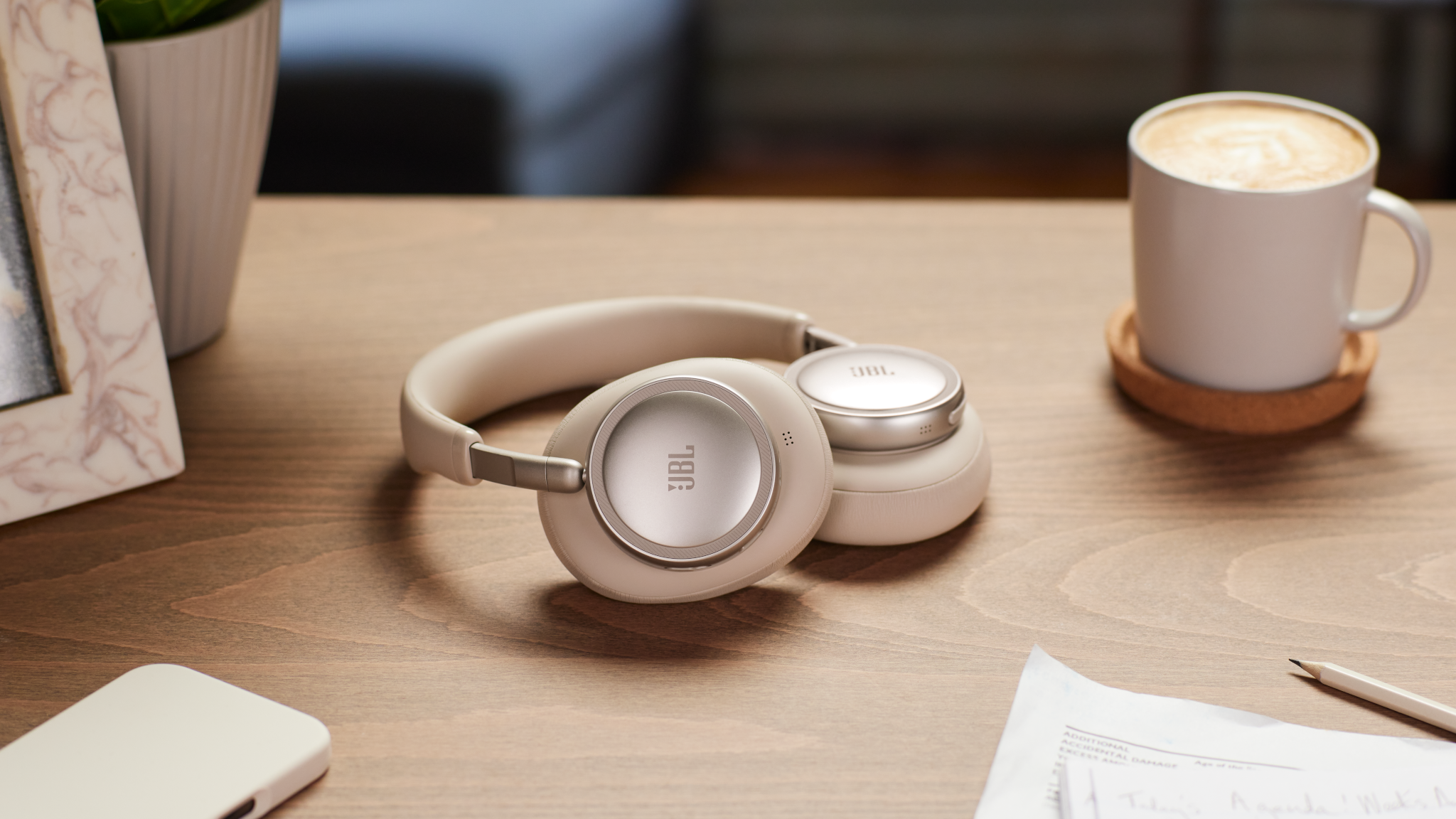 Cuffie beige con accenti argentati e logo JBL, accanto a una tazza di caffè.
