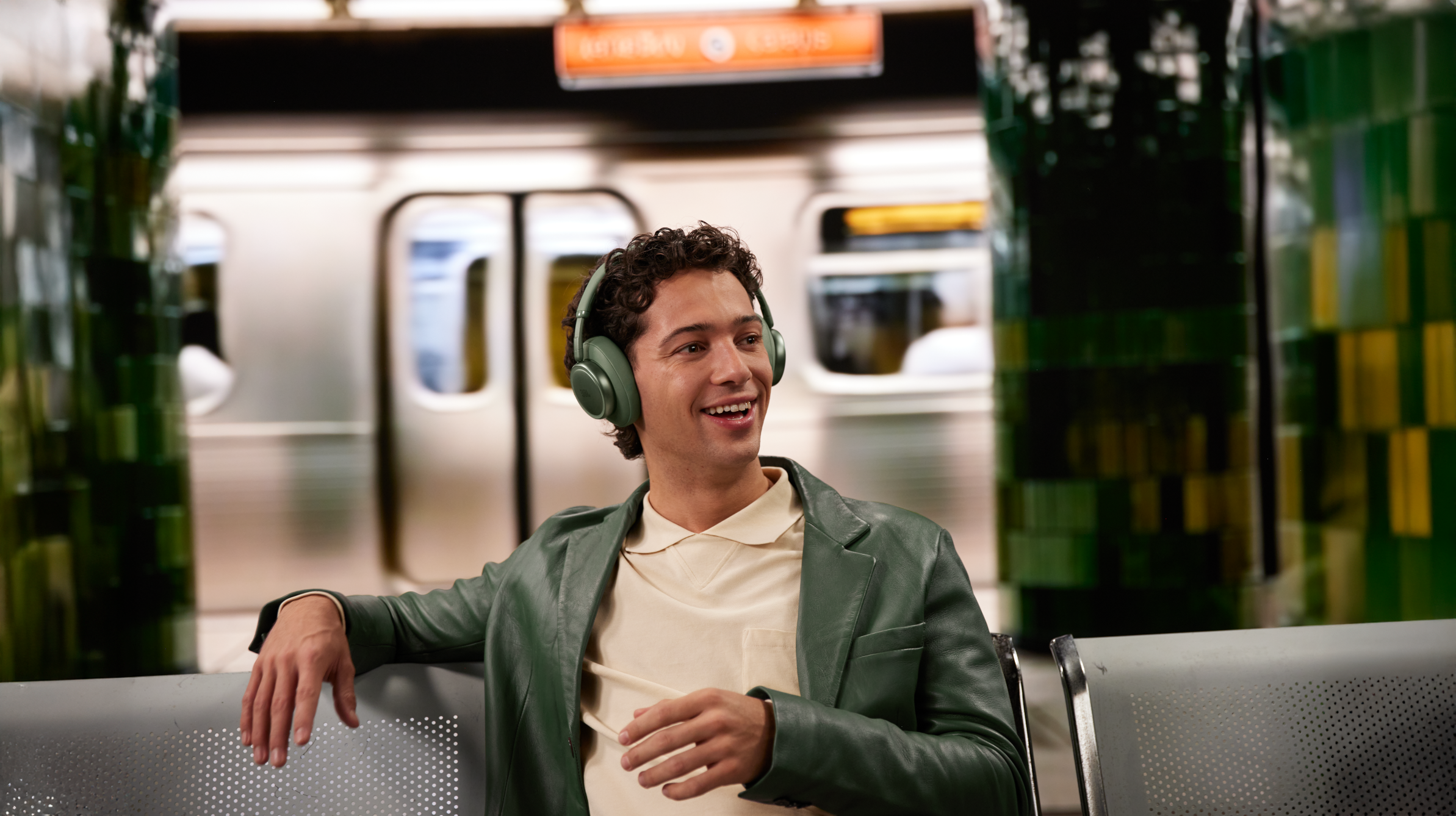 Ein Mann mit Kopfhörern sitzt im U-Bahn-Wagen und lächelt.