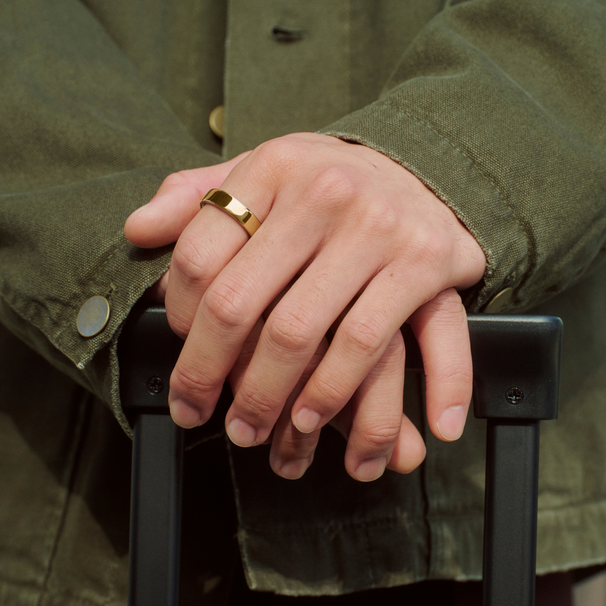 Eine Person in einem grünen Hemd trägt einen goldenen Ring und hält einen schwarzen Koffergriff.