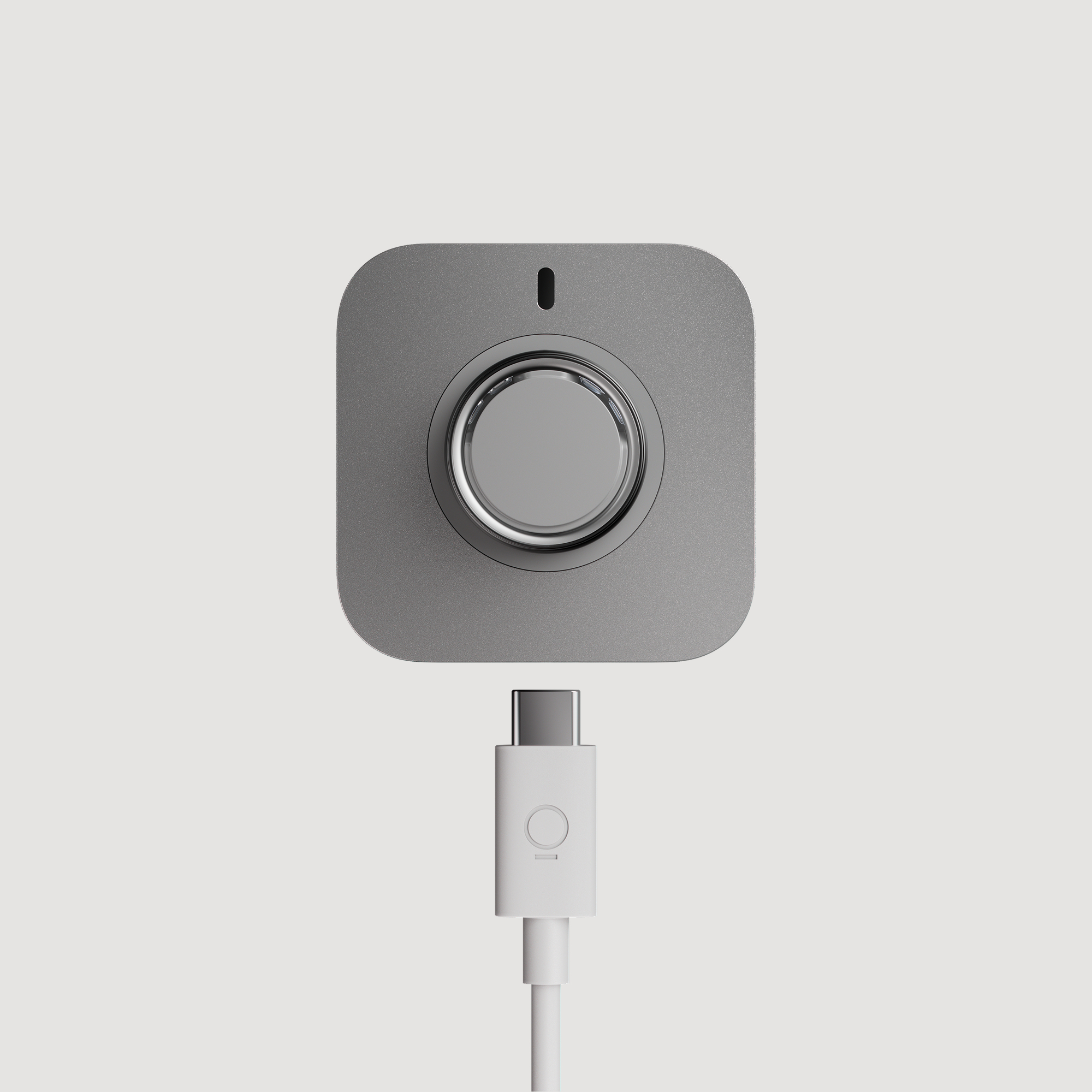 Ein silbernes quadratisches Ladegerät mit kreisförmiger Vertiefung, verbunden mit einem weißen USB-C-Kabel.