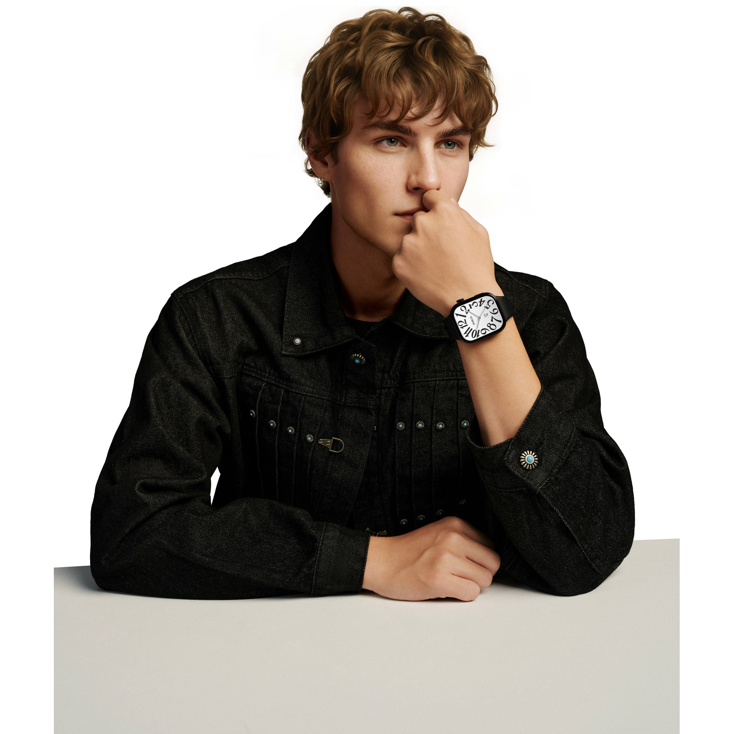Jonge man in een donker spijkerjack met een horloge om zijn pols zit aan tafel.