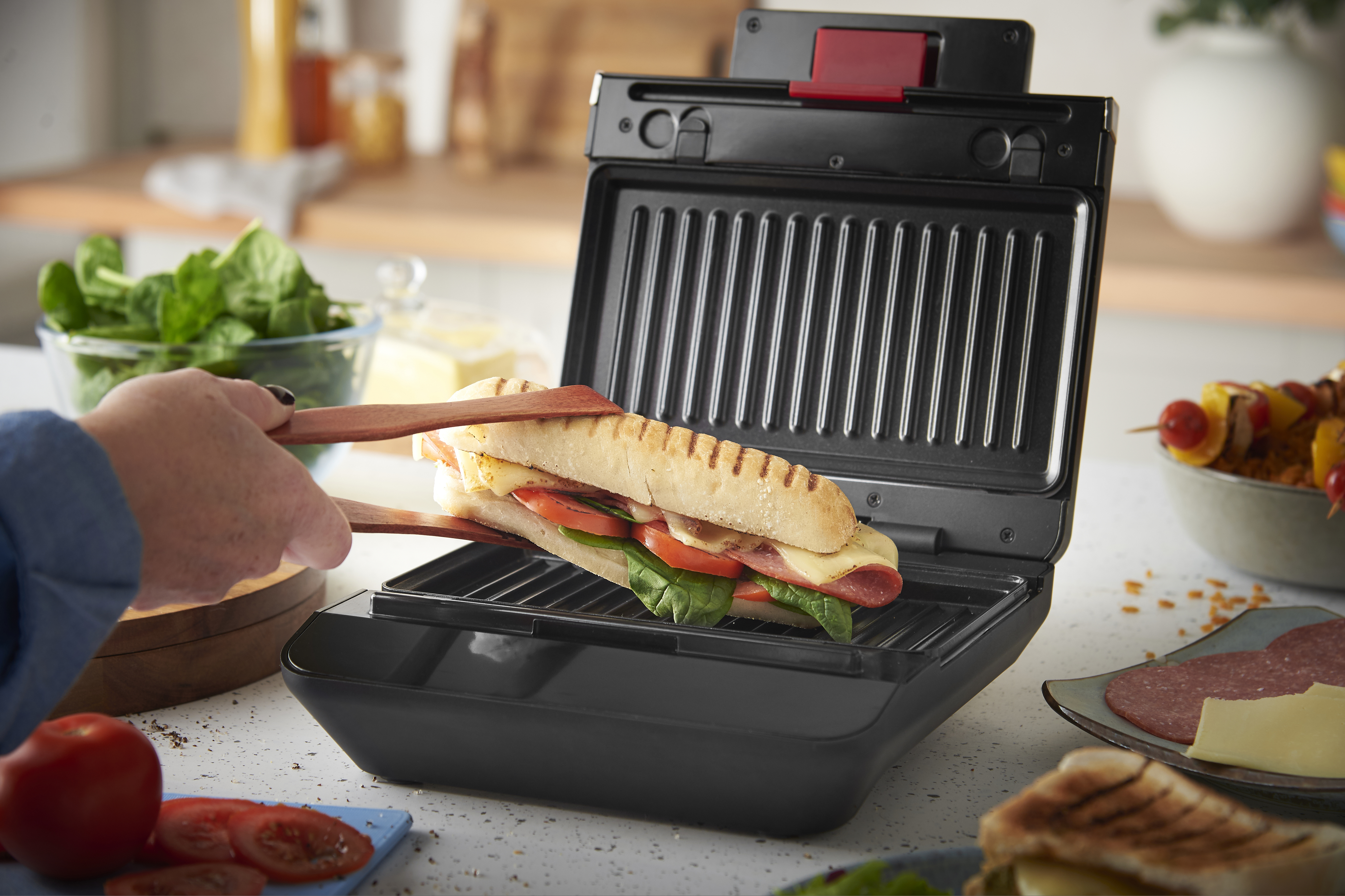 Ein Panini mit Fleisch, Käse, Tomaten und Spinat wird in einem Kontaktgrill zubereitet.