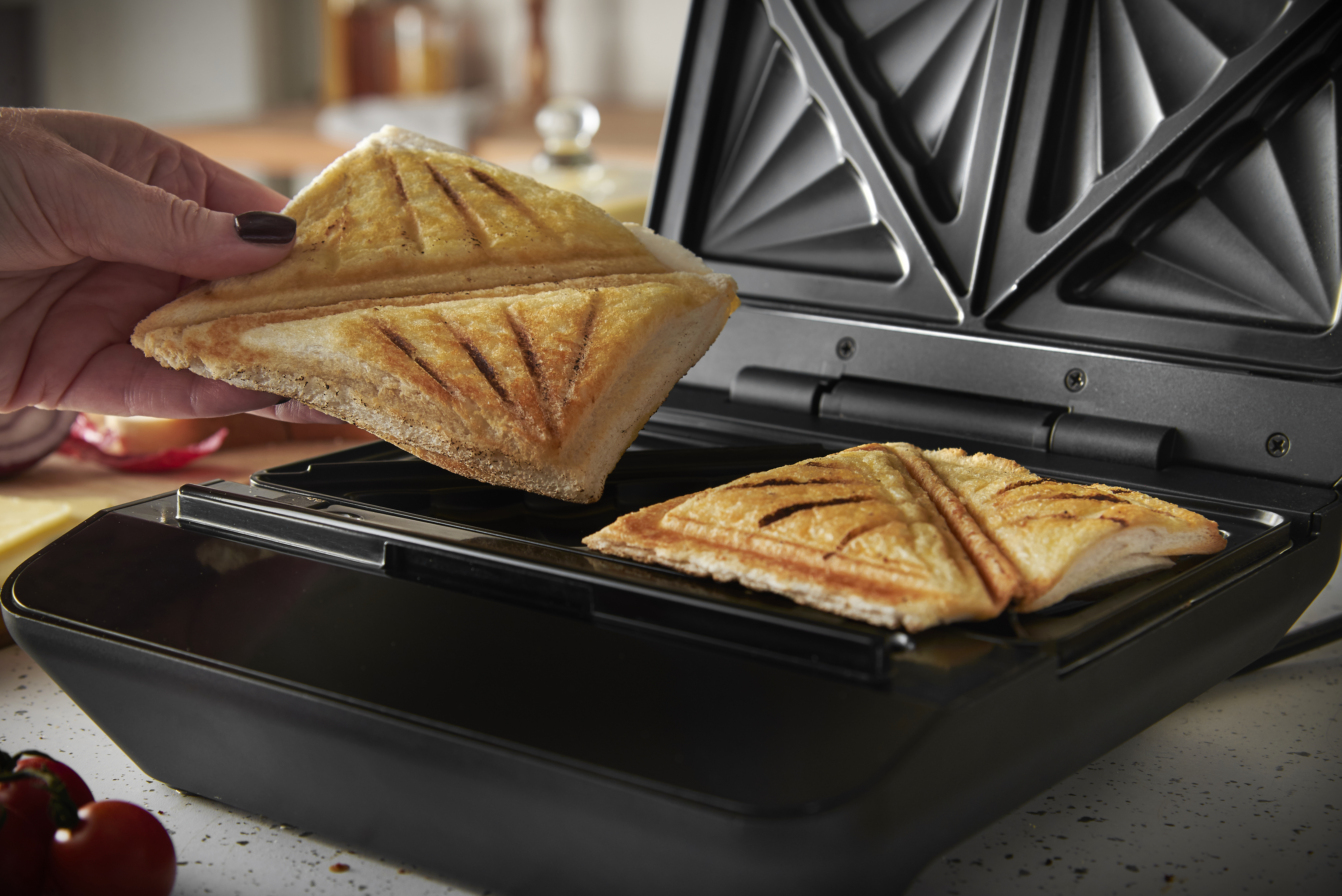 Eine Hand legt einen Toast in einen Sandwichmaker mit zwei Toastbroten.