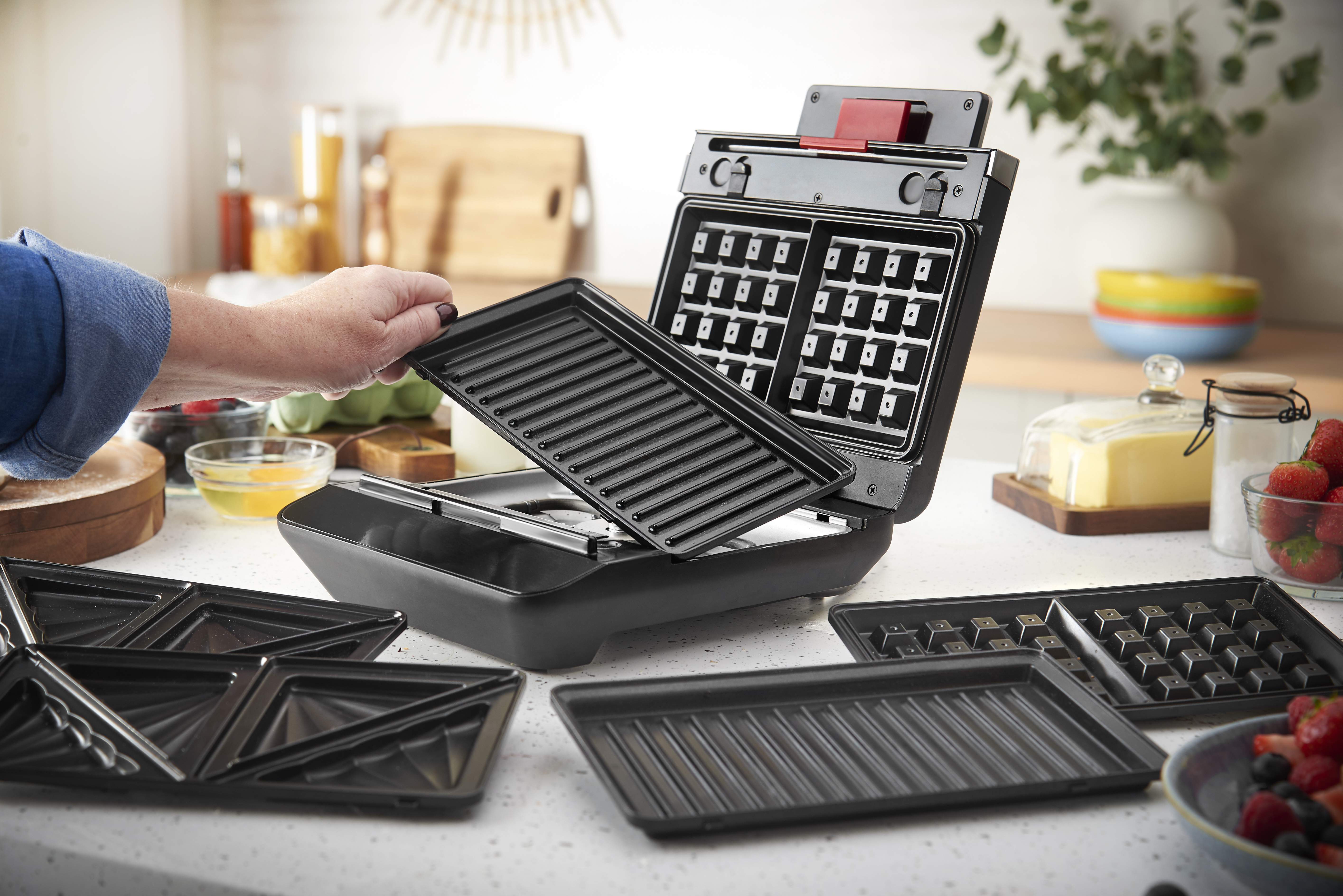 Ein Mann wechselt die Grillplatte eines offenen Sandwichmakers/Waffelautomaten.