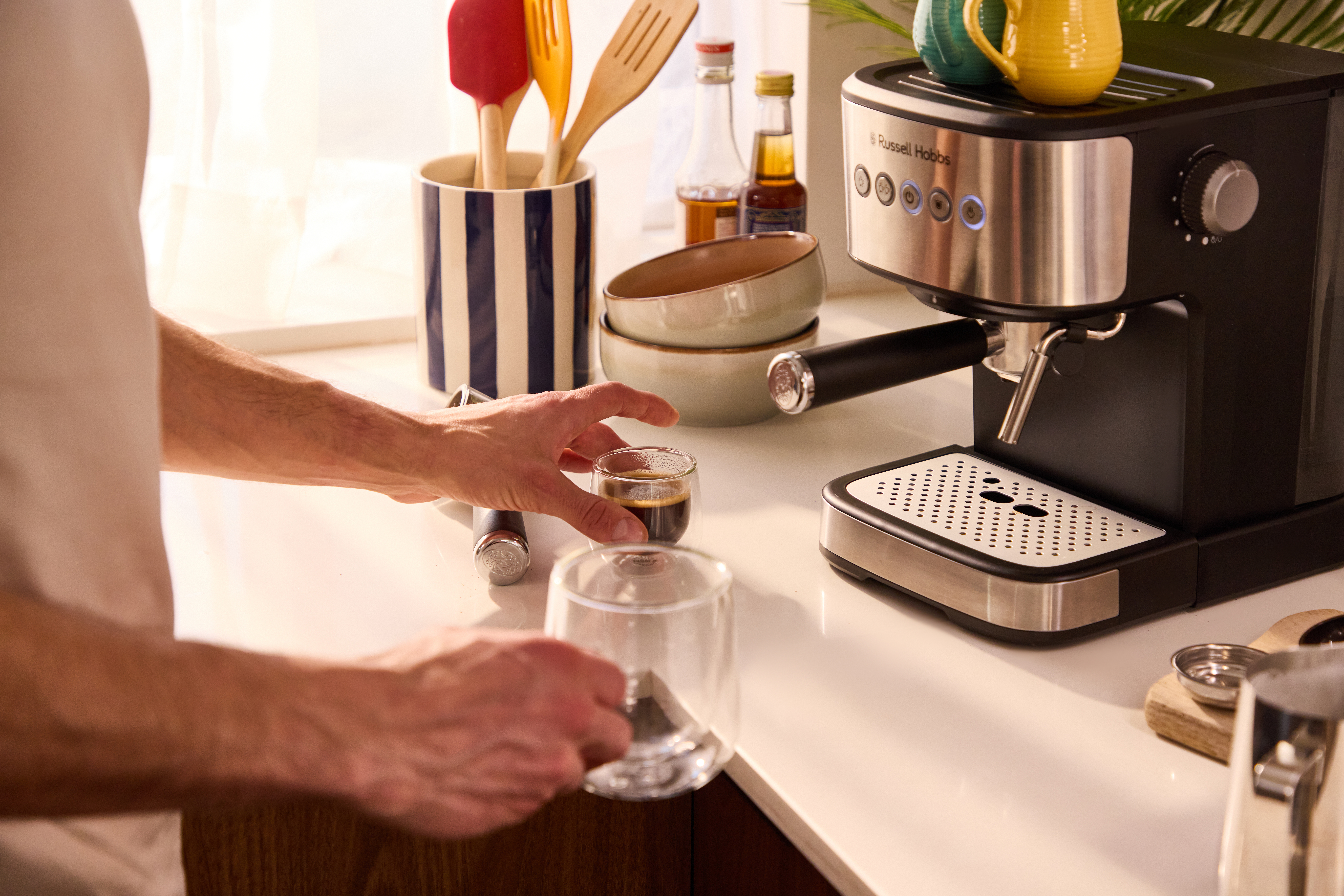 Eine Person bereitet Kaffee mit einer Espressomaschine zu, hält ein Glas mit Kaffee.