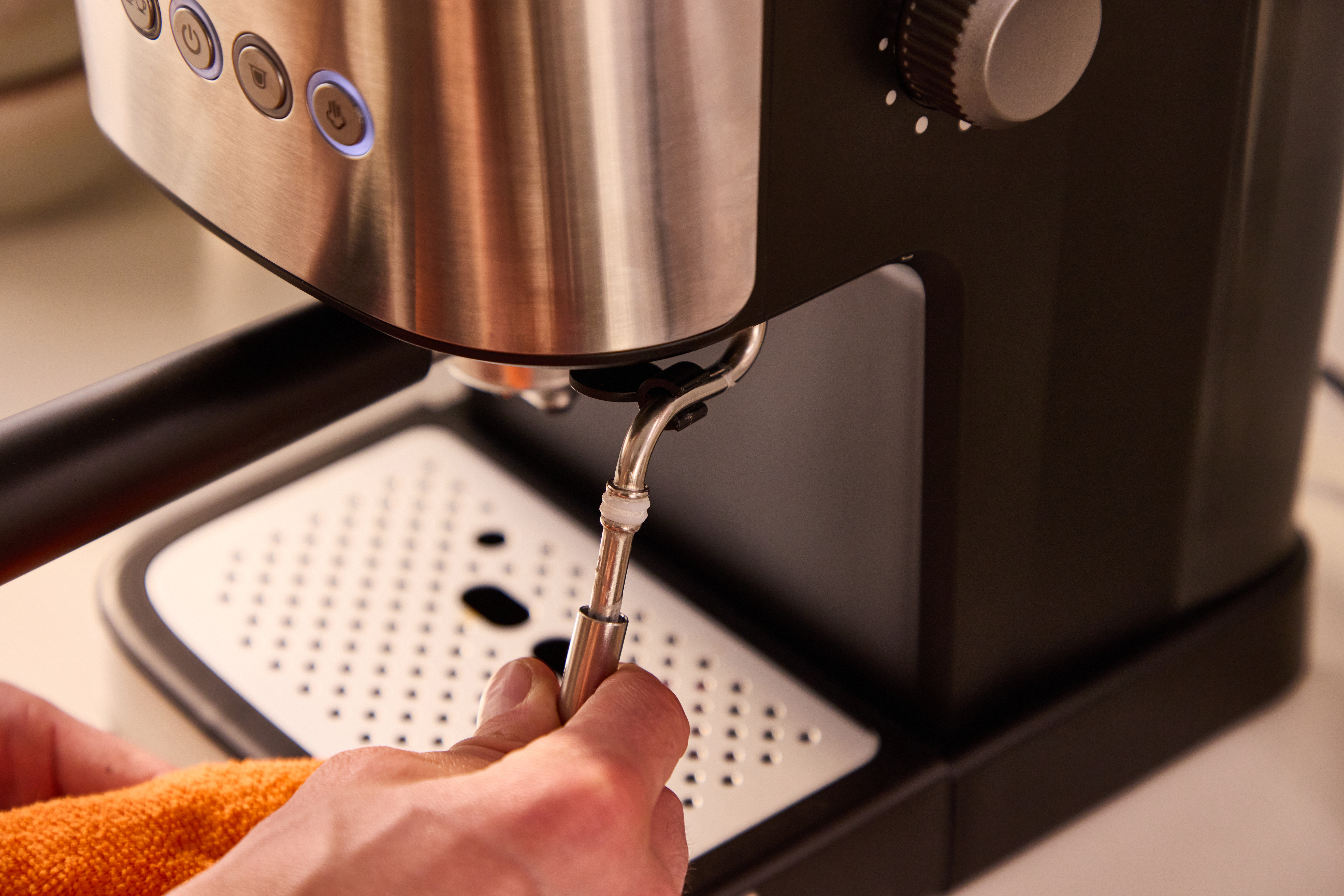 Eine Hand reinigt eine Kaffeemaschine mit einem orangefarbenen Tuch.
