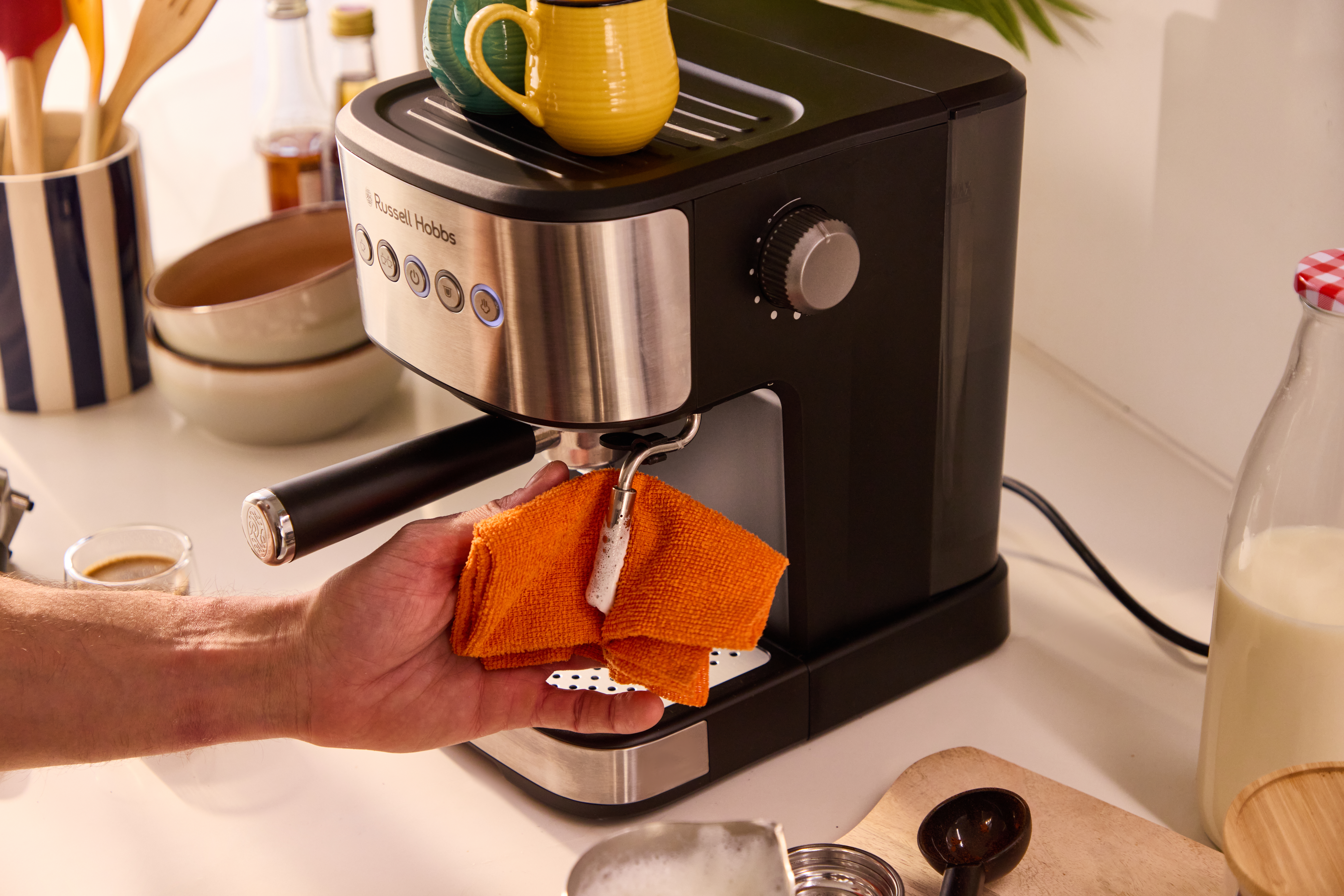 Eine Hand reinigt eine Espressomaschine mit einem orangenen Tuch.